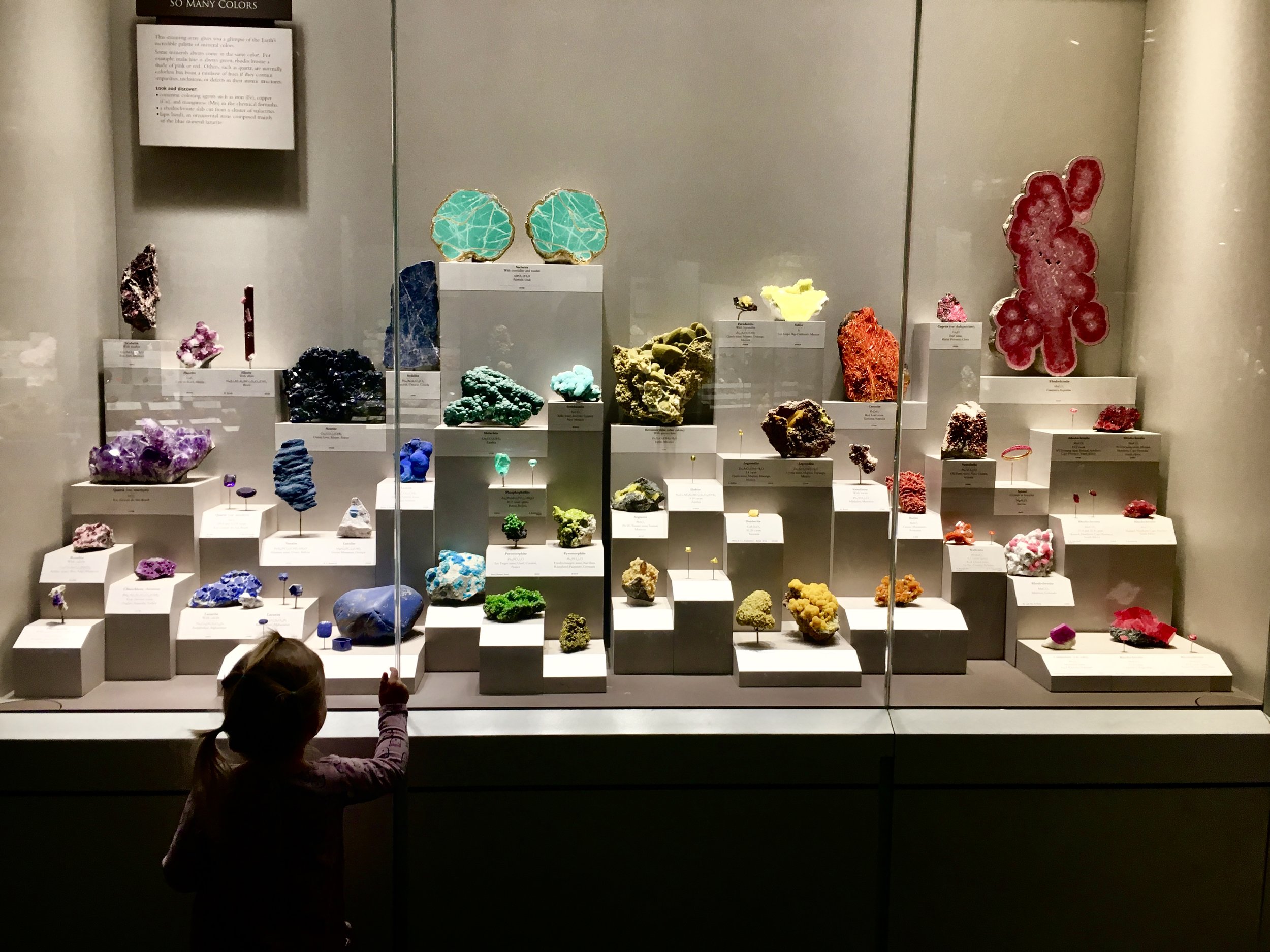 Image: A toddler in front of a display of colorful rocks and minerals