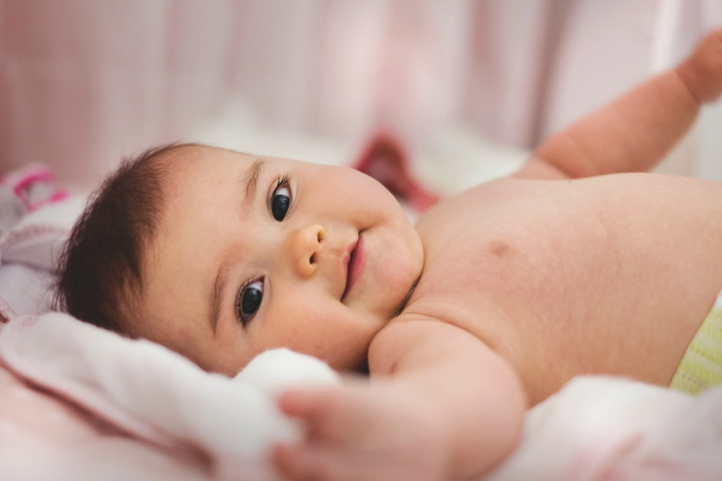 Image: A baby in a diaper is lying on a pink blanket and reaching for the camera. Image credit: Pexels