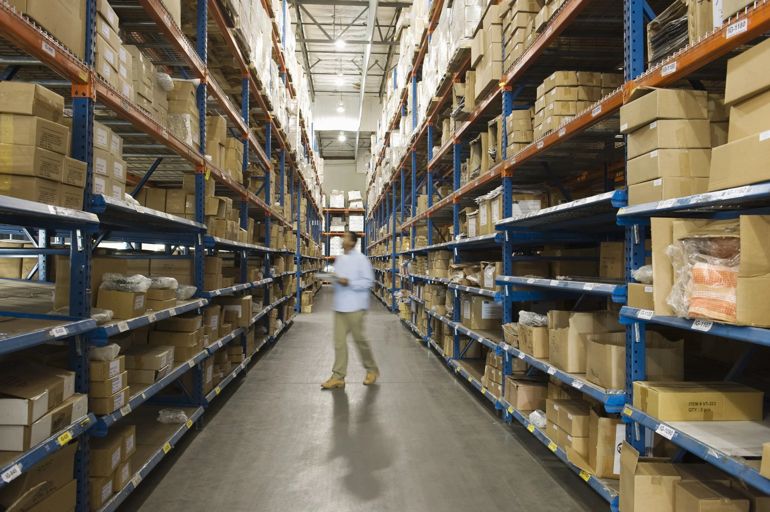 A man checks inventory in a warehouse full of boxes.