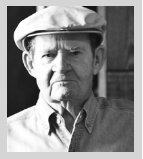 Black and white photo of an elderly man wearing a cap and a button-up shirt, looking directly at the camera with a serious expression.