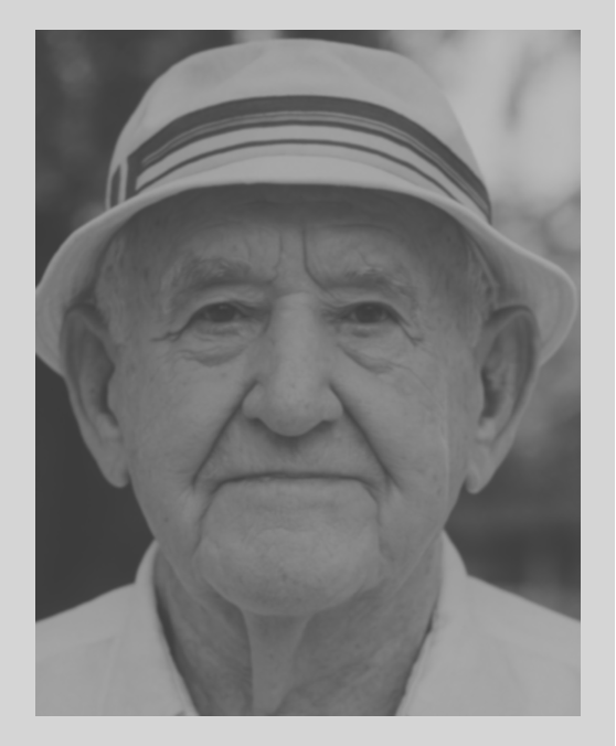 A close-up black-and-white photograph of an elderly man wearing a striped fedora hat and a collared shirt.