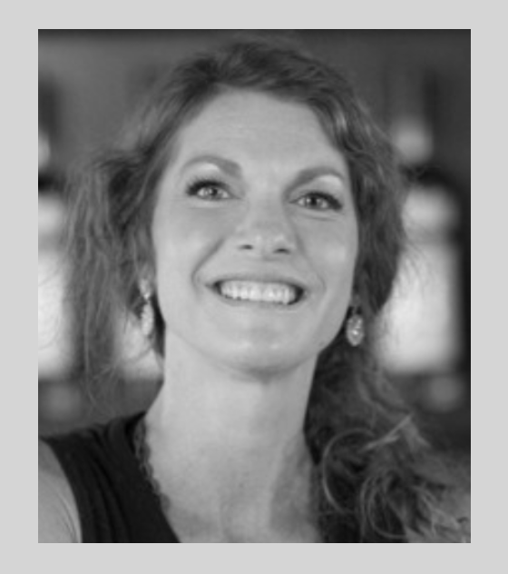 A woman with wavy hair smiling, wearing earrings, in black and white.