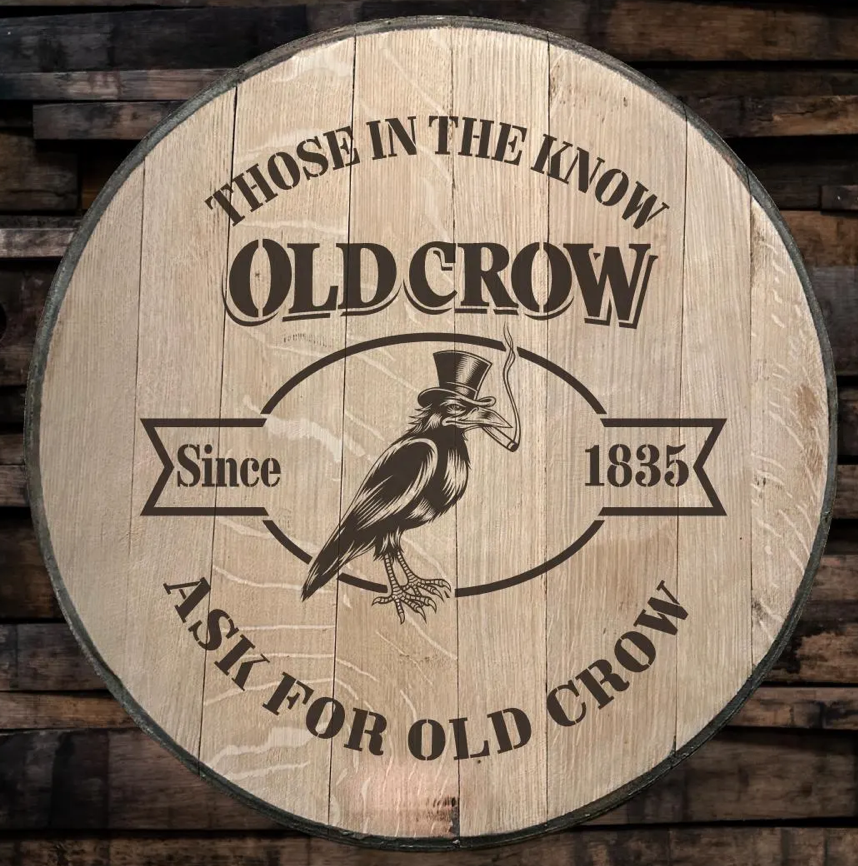 A round wooden sign with vintage-style text and illustration. It reads 'Those in the know Old Crow since 1835, a sip for old crow.' The sign features an illustration of a crow wearing a top hat, with a cigar in its beak, sitting inside an oval border.
