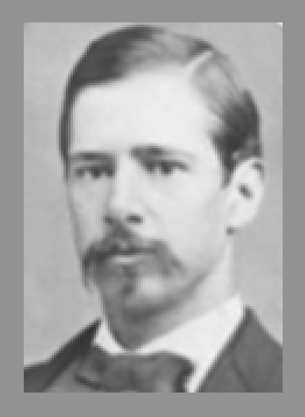 Portrait of a man with a mustache and side-parted hair, wearing a tuxedo.