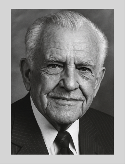 Black and white portrait of an elderly man with white hair, wearing a suit and tie, smiling slightly.