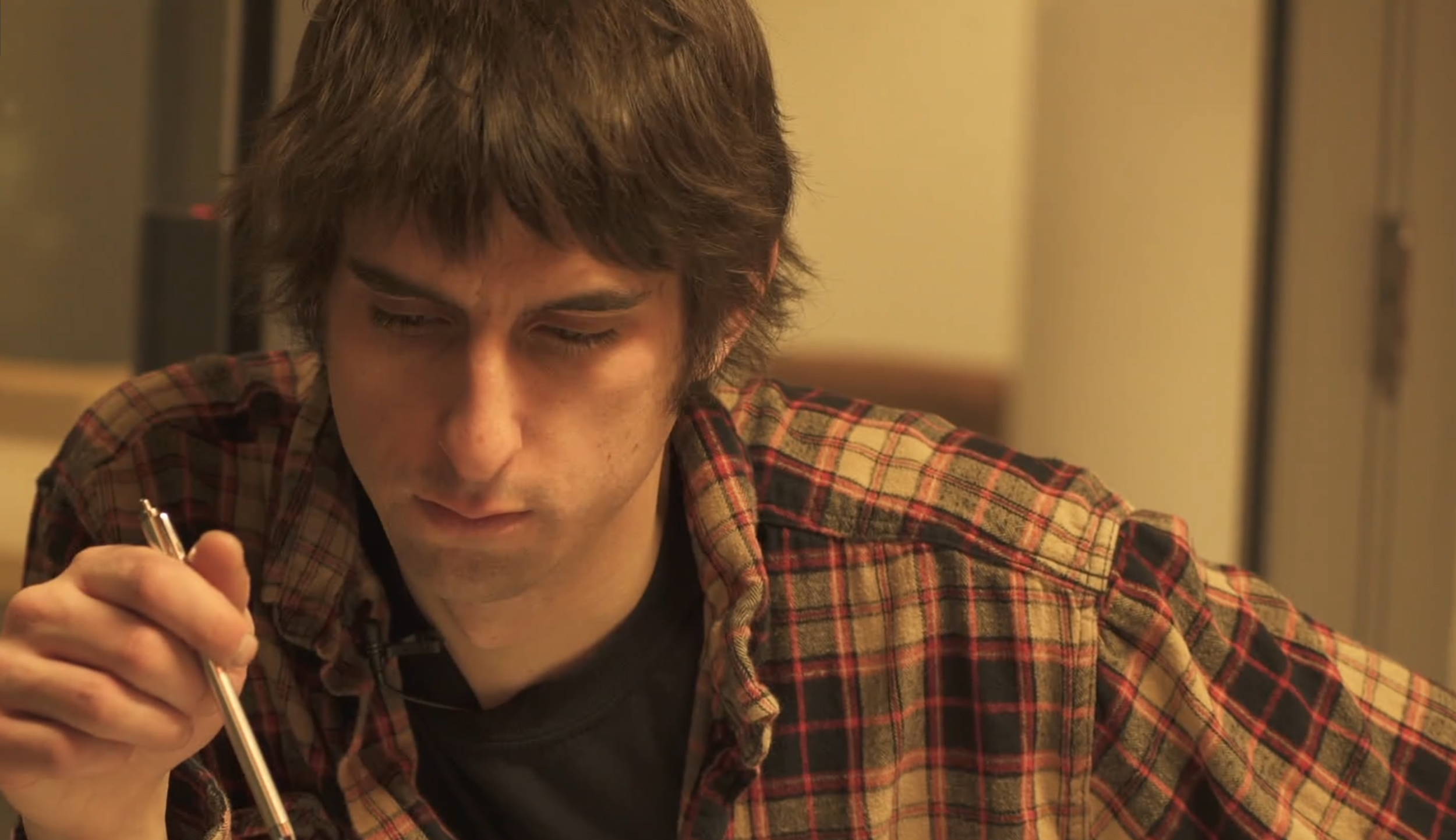 A young man holding a pen looks down in concentration