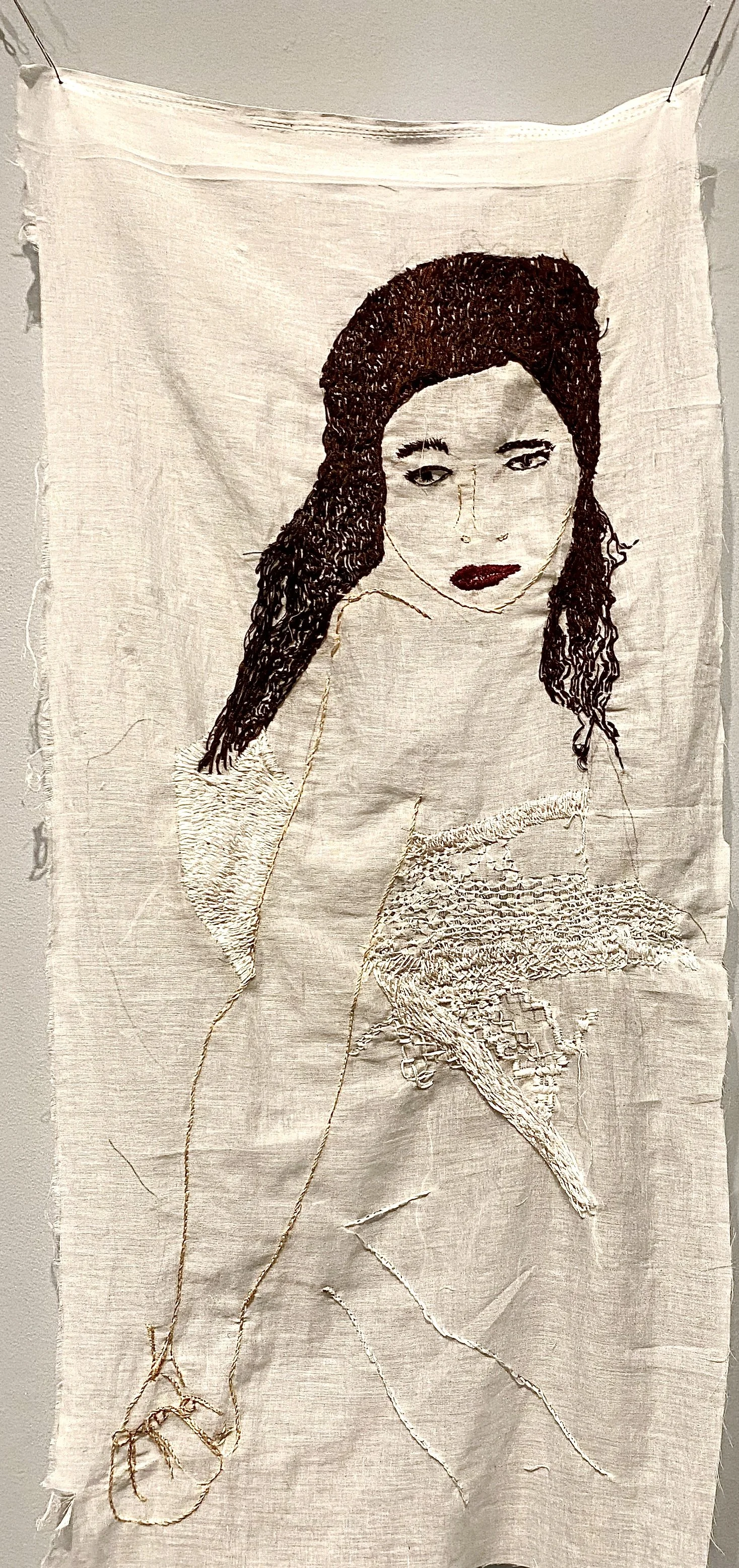 Textile art featuring an embroidered portrait of a woman with dark hair on fabric.