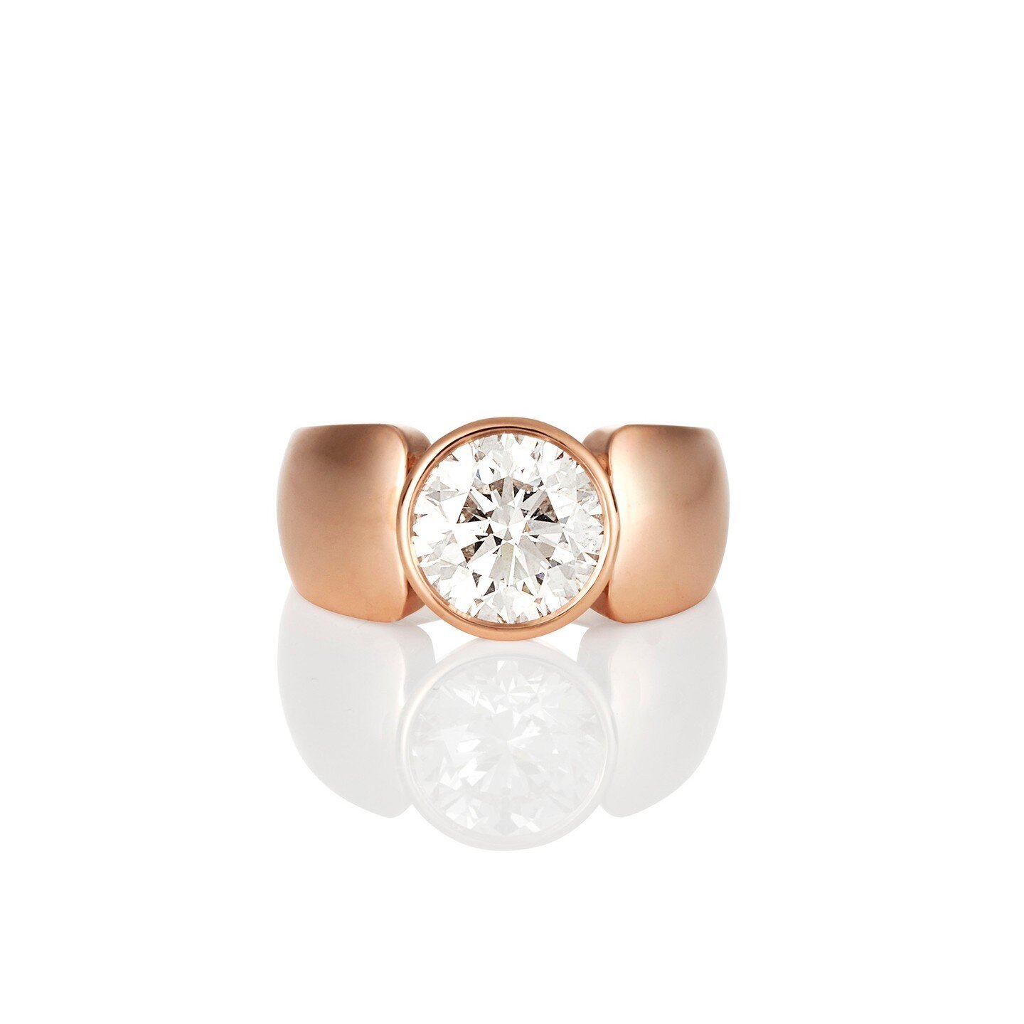 A 2.5 carat round brilliant diamond steals the show on this simple modern bezel set wide solitaire engagement ring. Set in 18 karat rose gold.