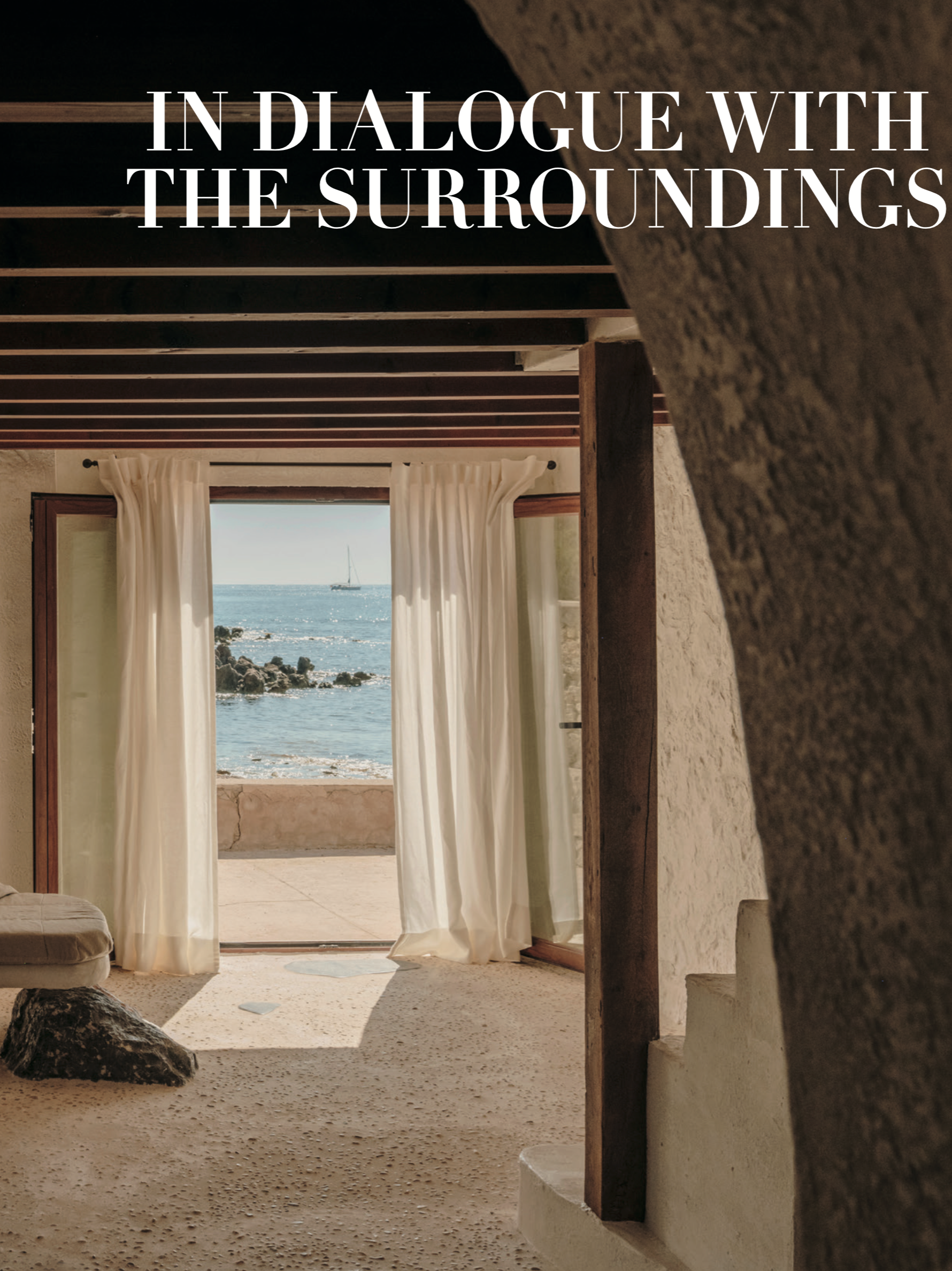 Open door with sheer white curtains, revealing a view of the ocean with a sailboat and rocky shoreline.