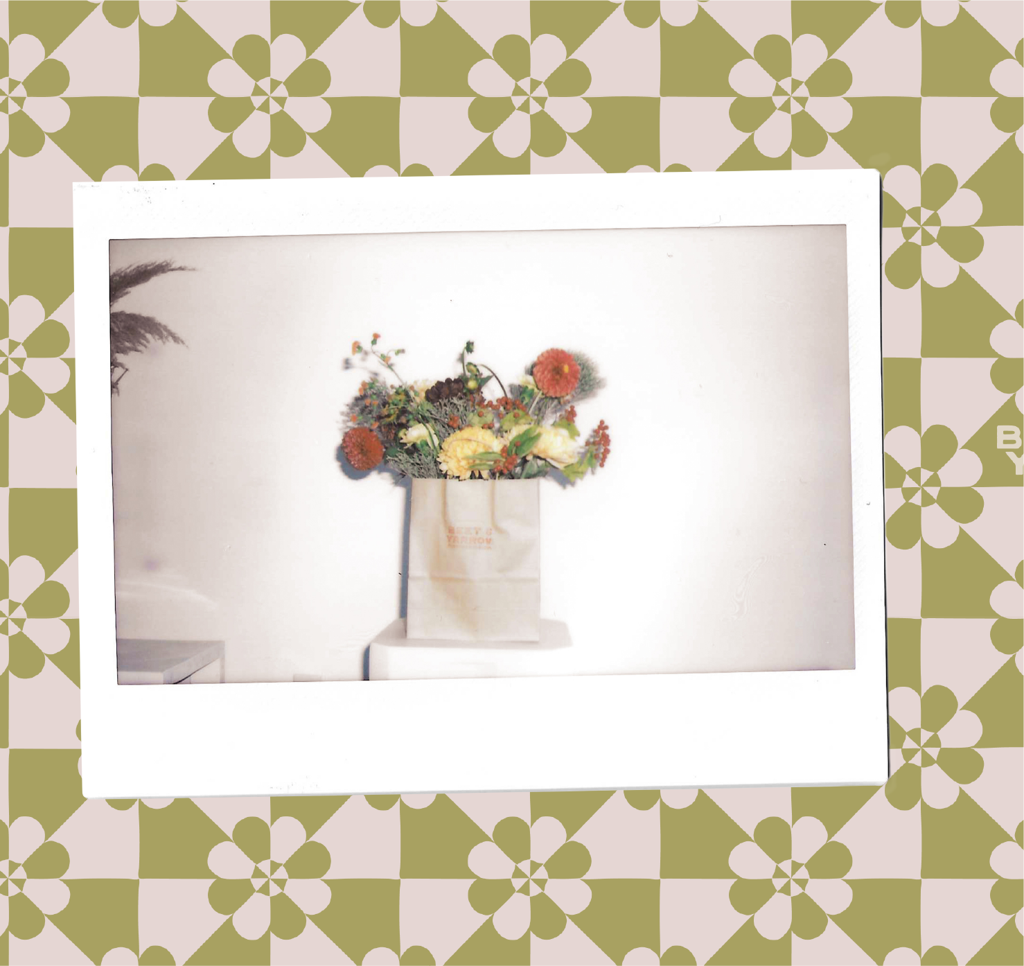 Polaroid Photo of a red and green floral arrangement inside of a stamped kraft bag sitting on top of a white pedestal. The Polaroid is overlayed on top of a quilt floral design