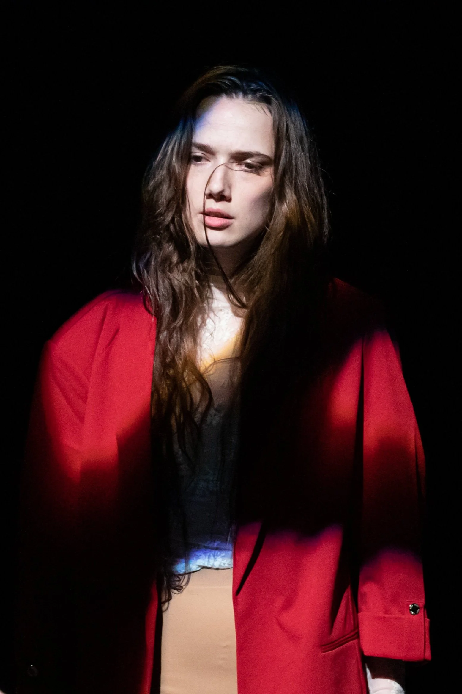 morgaine, a white dancer with long brown hair stares hopelessly into the foreground. red blazer on their shoulders. strand of hair clings to their face.