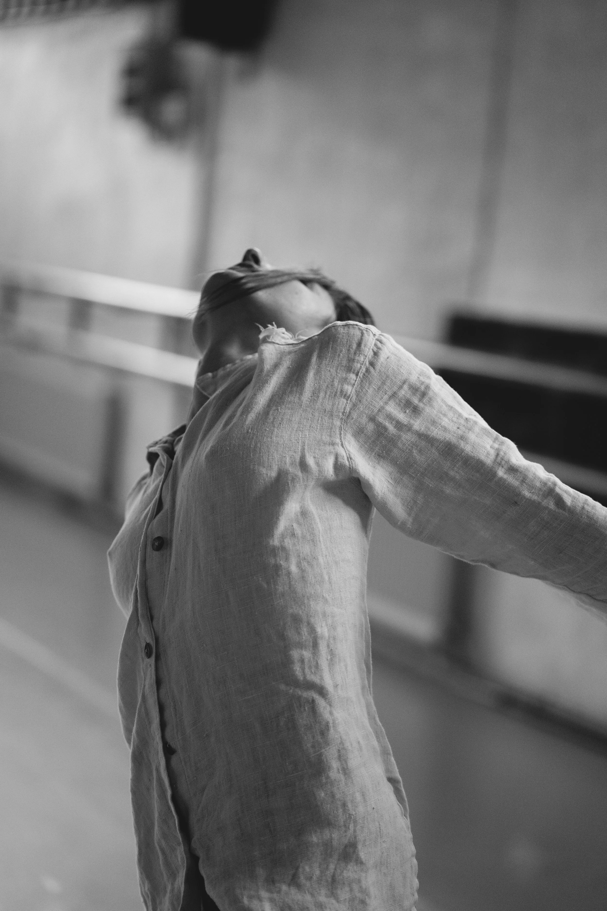Black and white image of Anna in a barn studio in motion. Chest lifted in a torn up button down top.