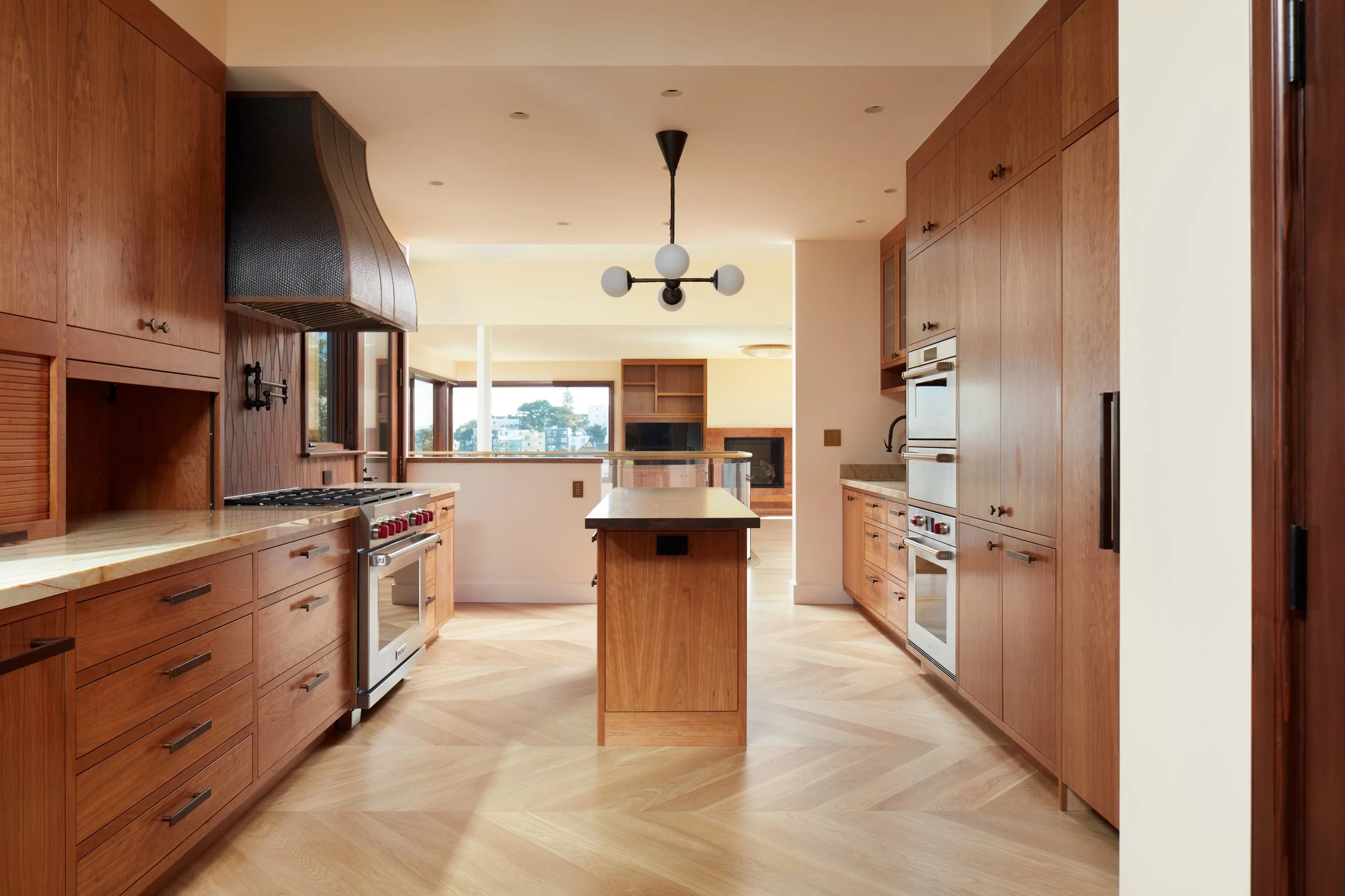 Modern kitchen with wooden cabinets, a black range hood, a small kitchen island, and large windows overlooking a city view.