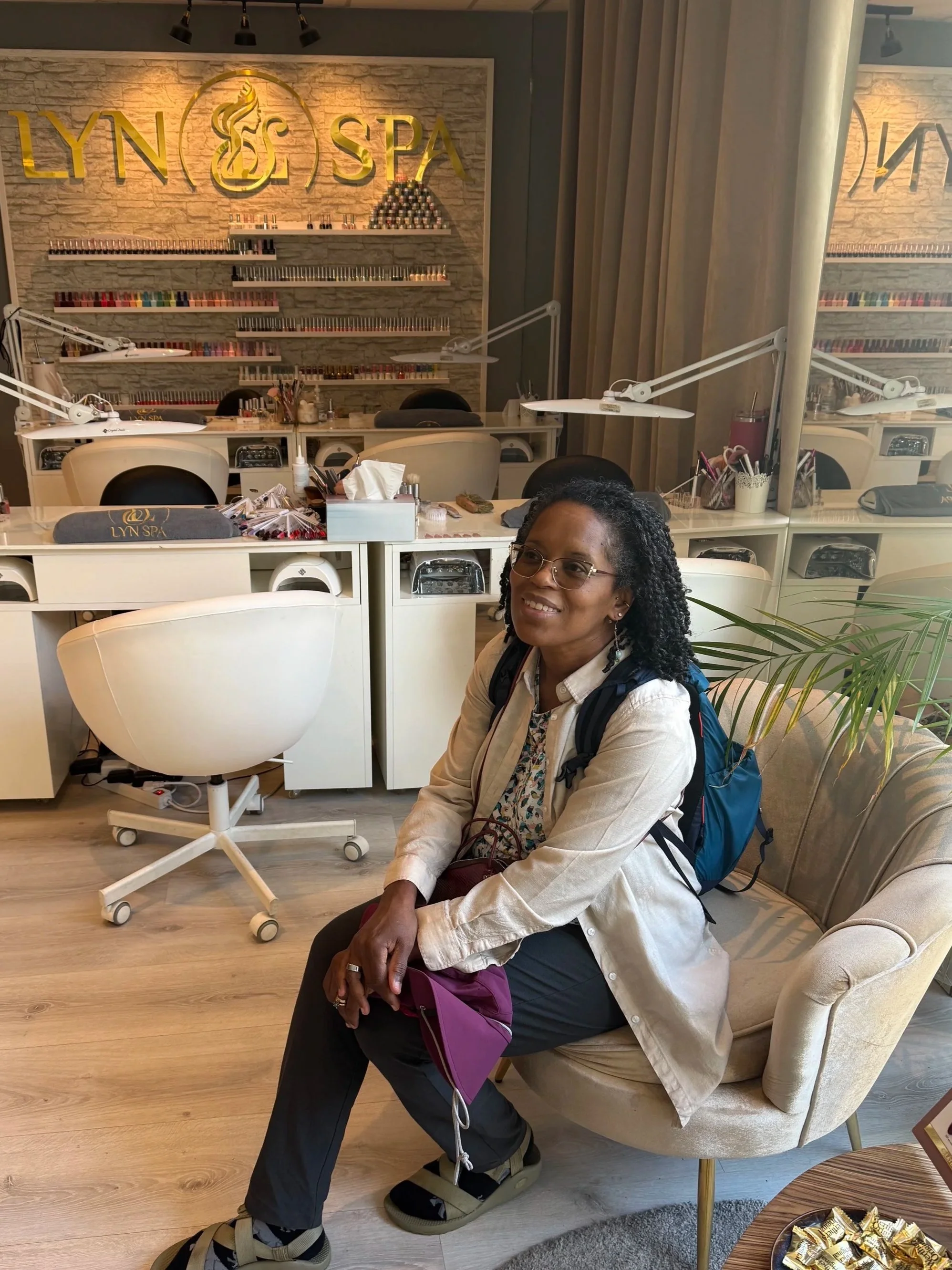 Woman sewed in a plush chair in front of a sign with the Lyn Spa logo and title.