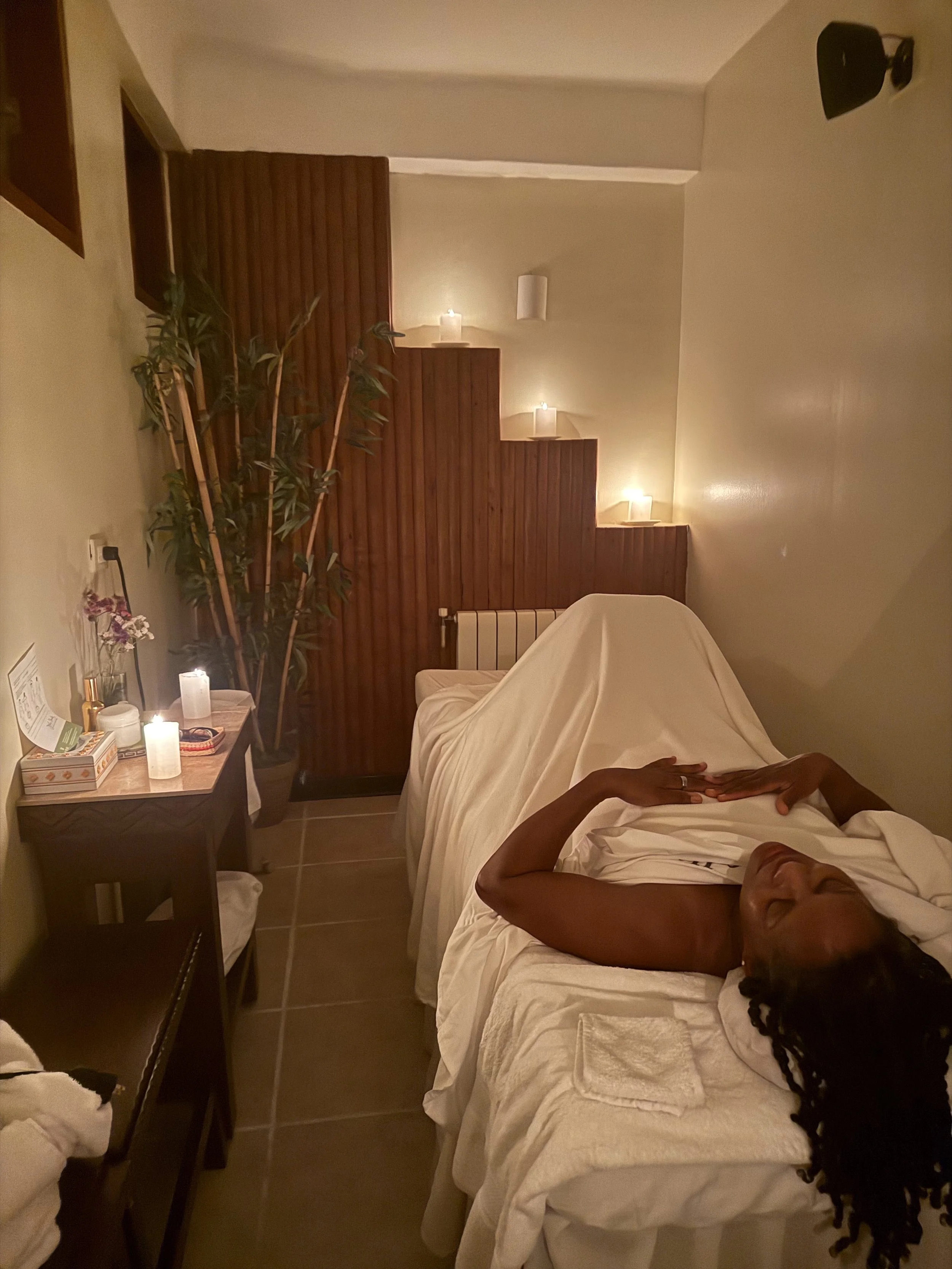 Massage table dressed in white linens.  woman lying on the massage table with hands clasped on abdomen.