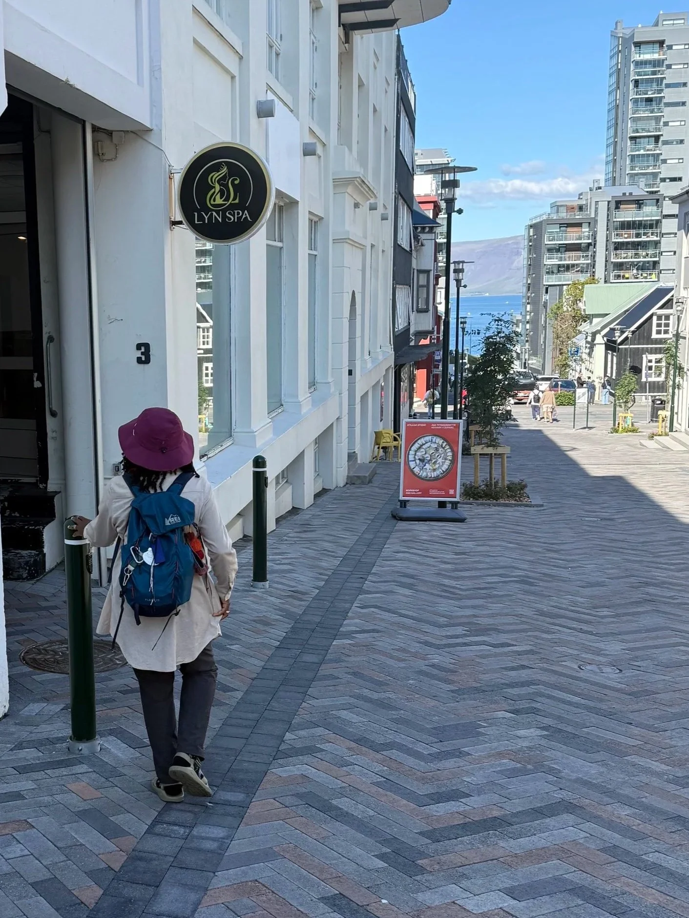 Woman wearing a maroon hat walking down a hill towards a shop with a store sign of Lyn Spa