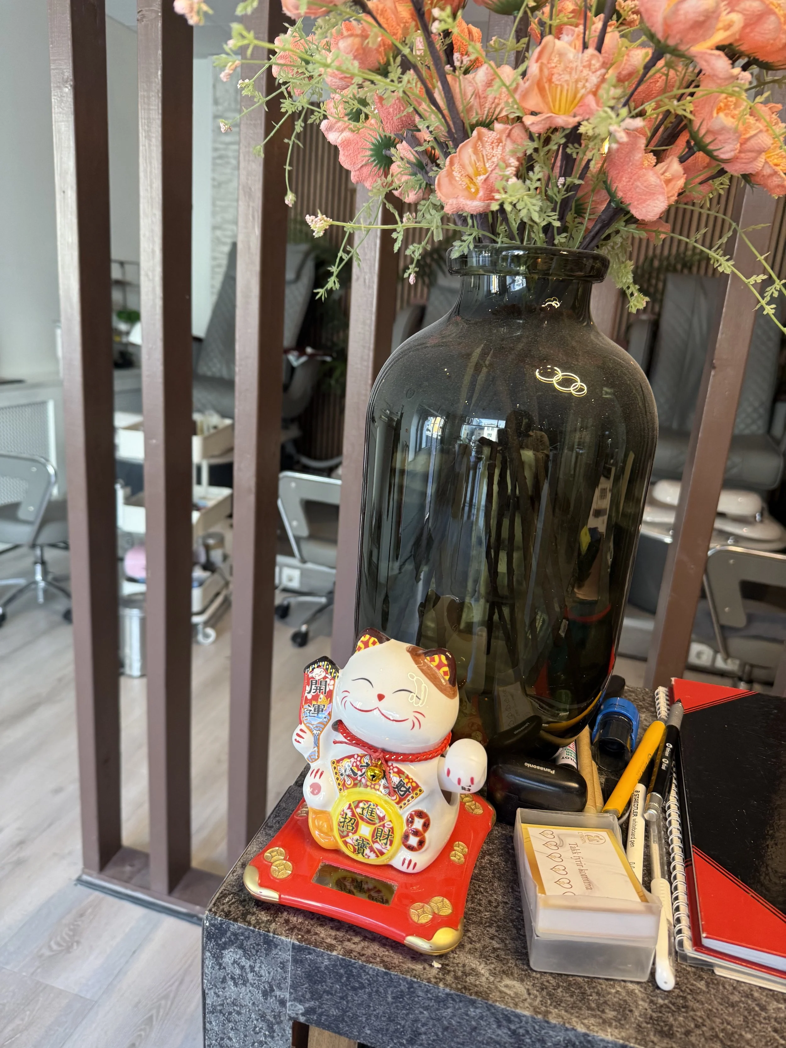 Happy cat on table beside a large vase filled with orange flowers.  Pedicure chairs in the background.
