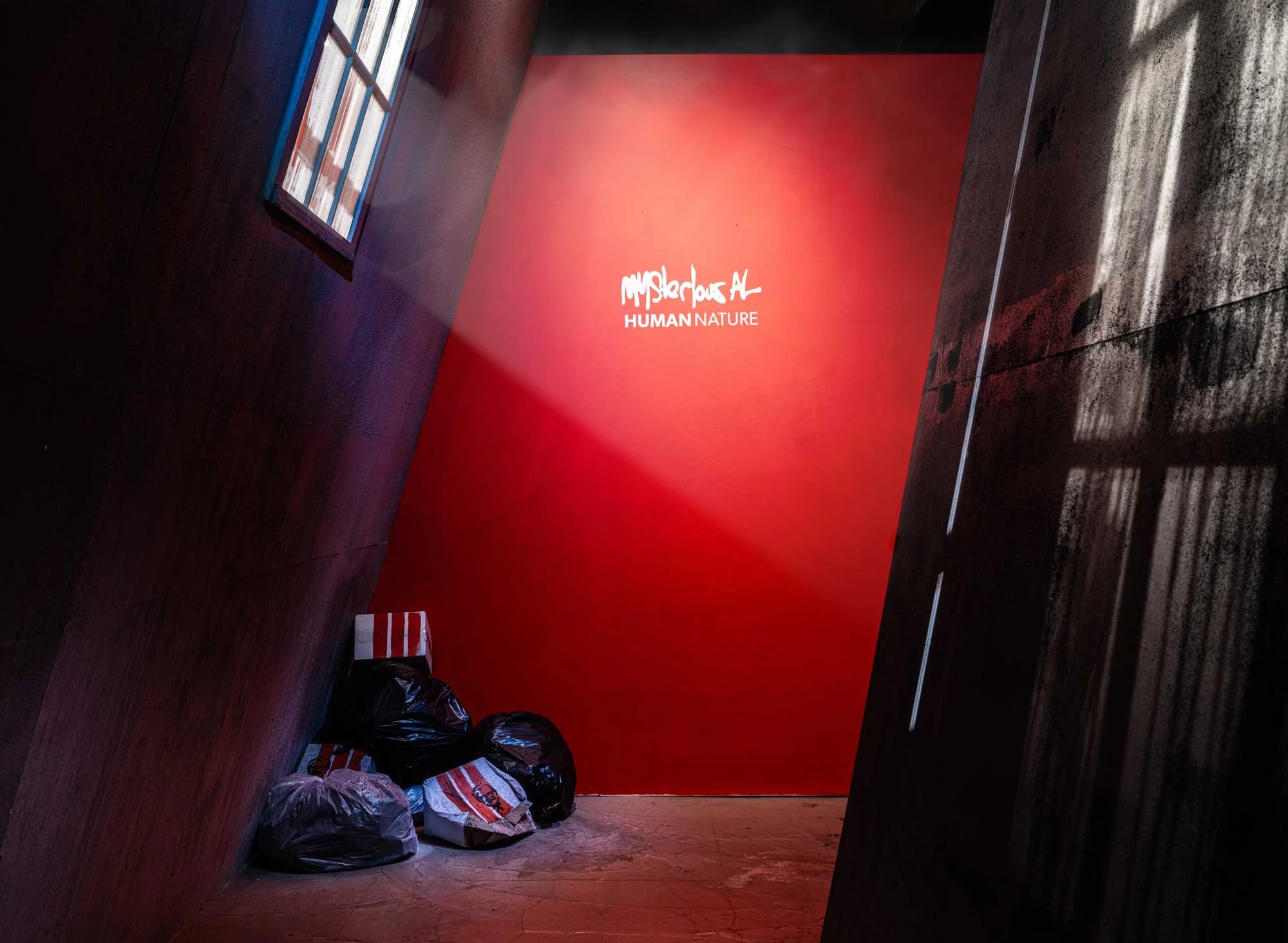 A dark alley with a red wall displaying the words "MYSTERIOUS AL Human Nature" and several trash bags on the ground. Mysterious al immersive pop up art exhibition Human Nature, Art in disused warehouse, pop-up spaces, colourful, striking contemporary