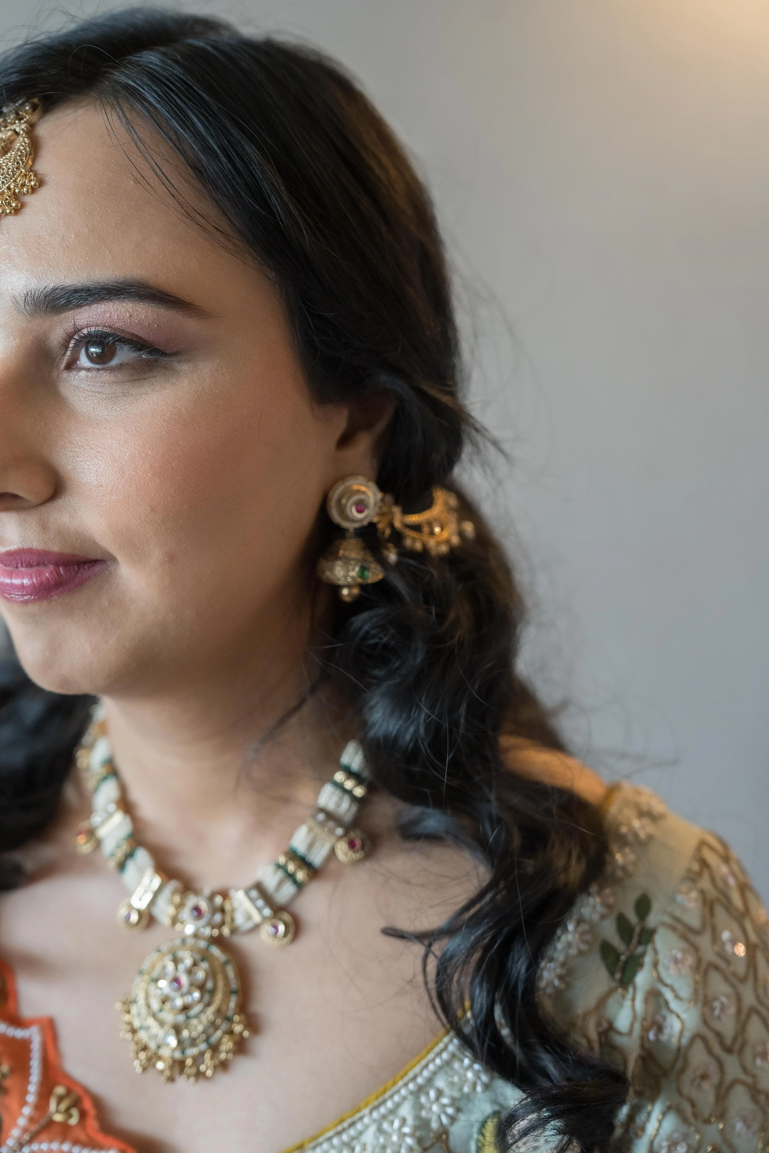 Close-up of a bride wearing traditional Indian jewelry and clothing, with dark wavy hair and a light makeup look.