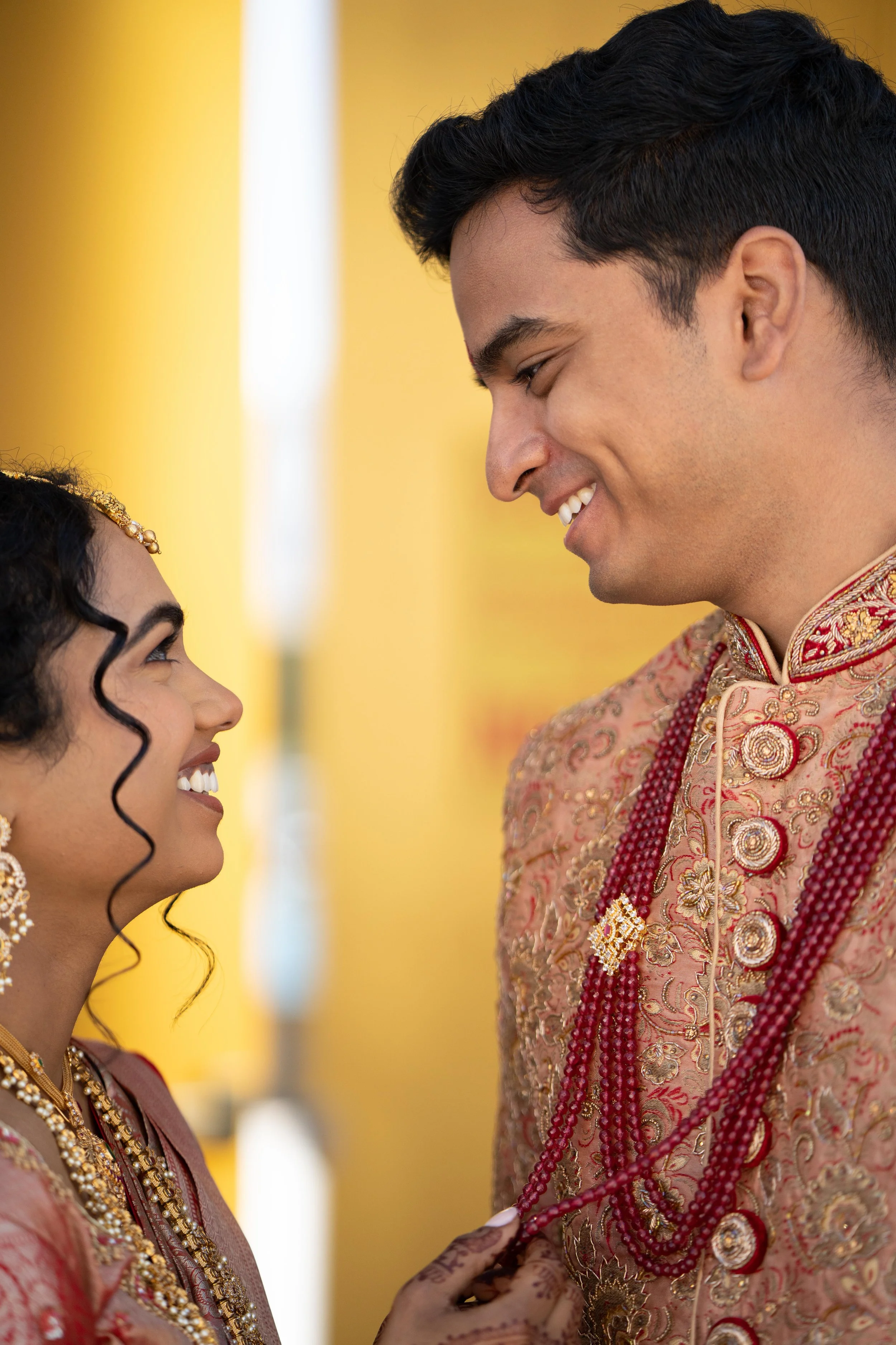 A bride and groom looking at each other smiling during a traditional Indian wedding ceremony.