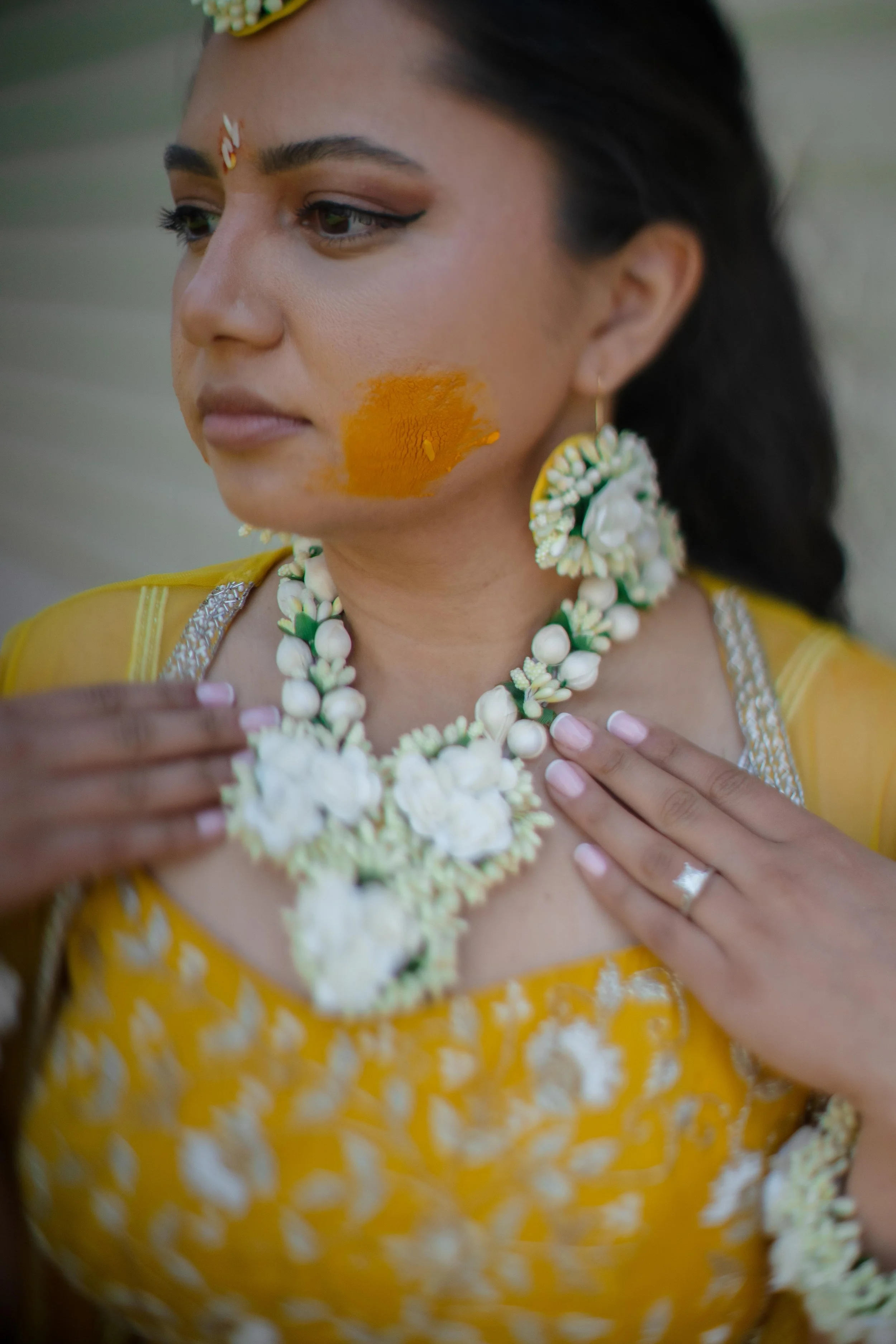 Close-up of a bride wearing traditional yellow attire and ornate jewelry, with an orange powder on her cheek, likely during a cultural or religious celebration.