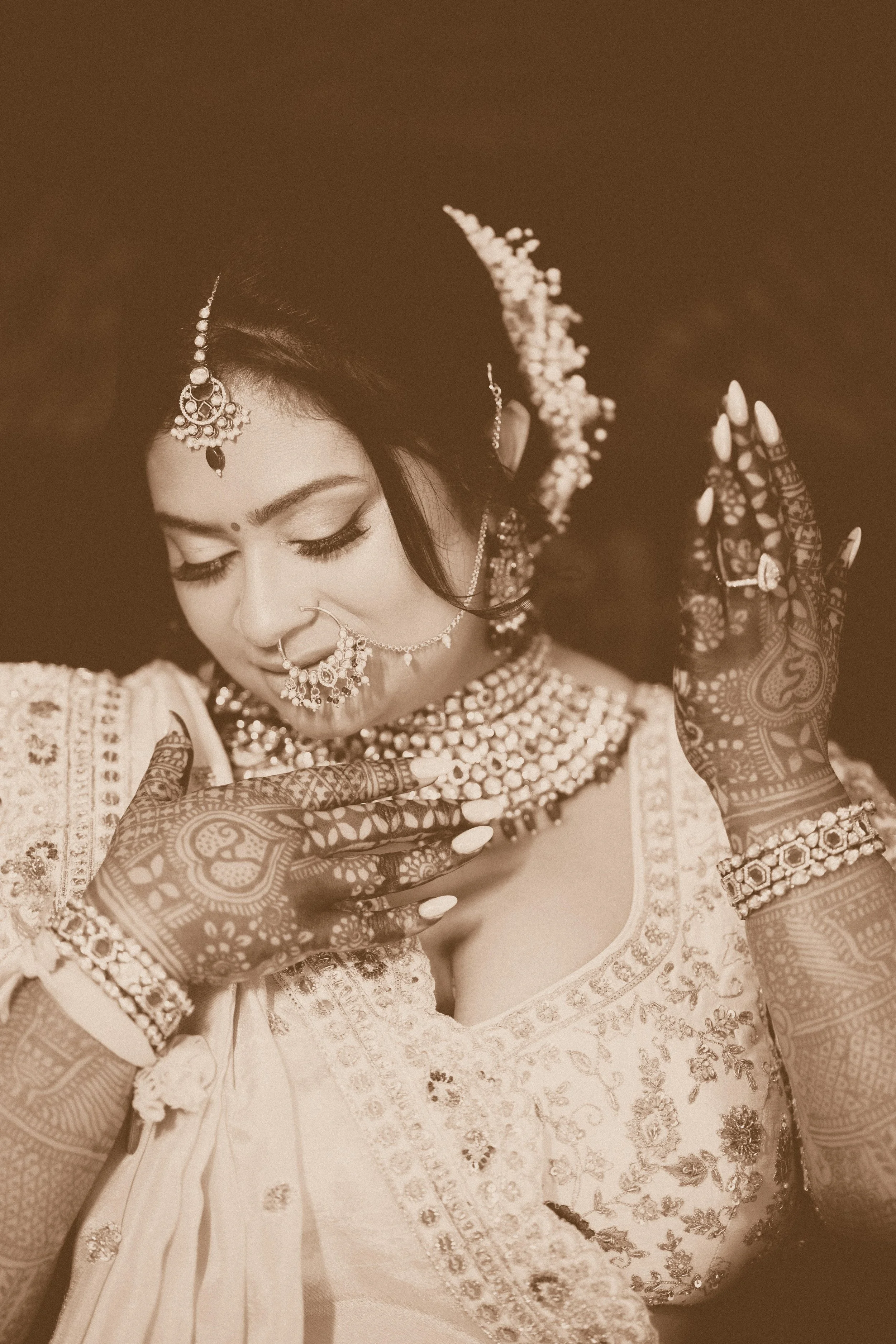 A Bride dressed in traditional Indian attire with intricate jewelry and henna on her hands, posing with her eyes closed.