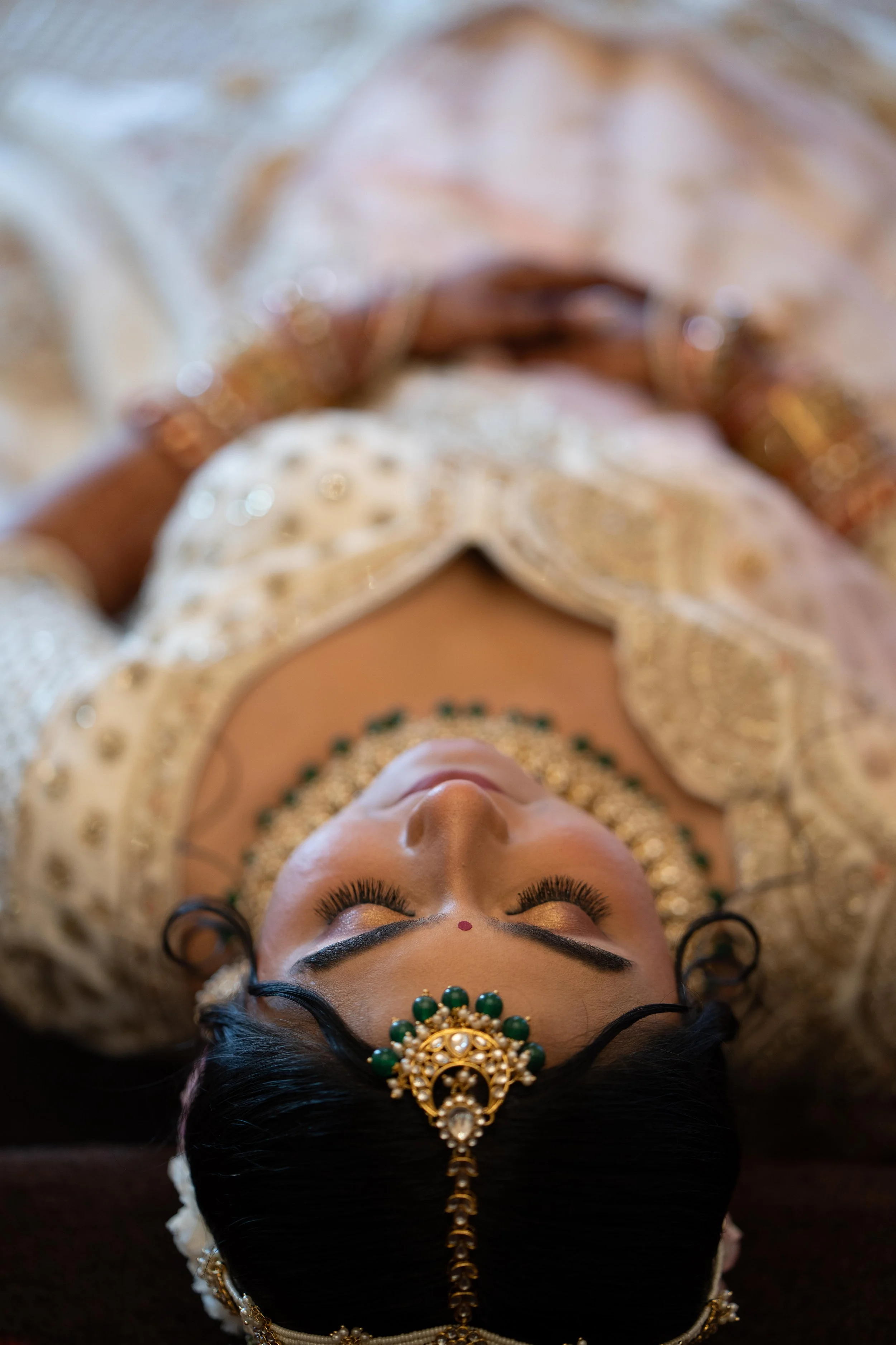 A Bride dressed in traditional Indian wedding attire, lying down with her eyes closed, wearing intricate jewelry and a richly embroidered outfit.