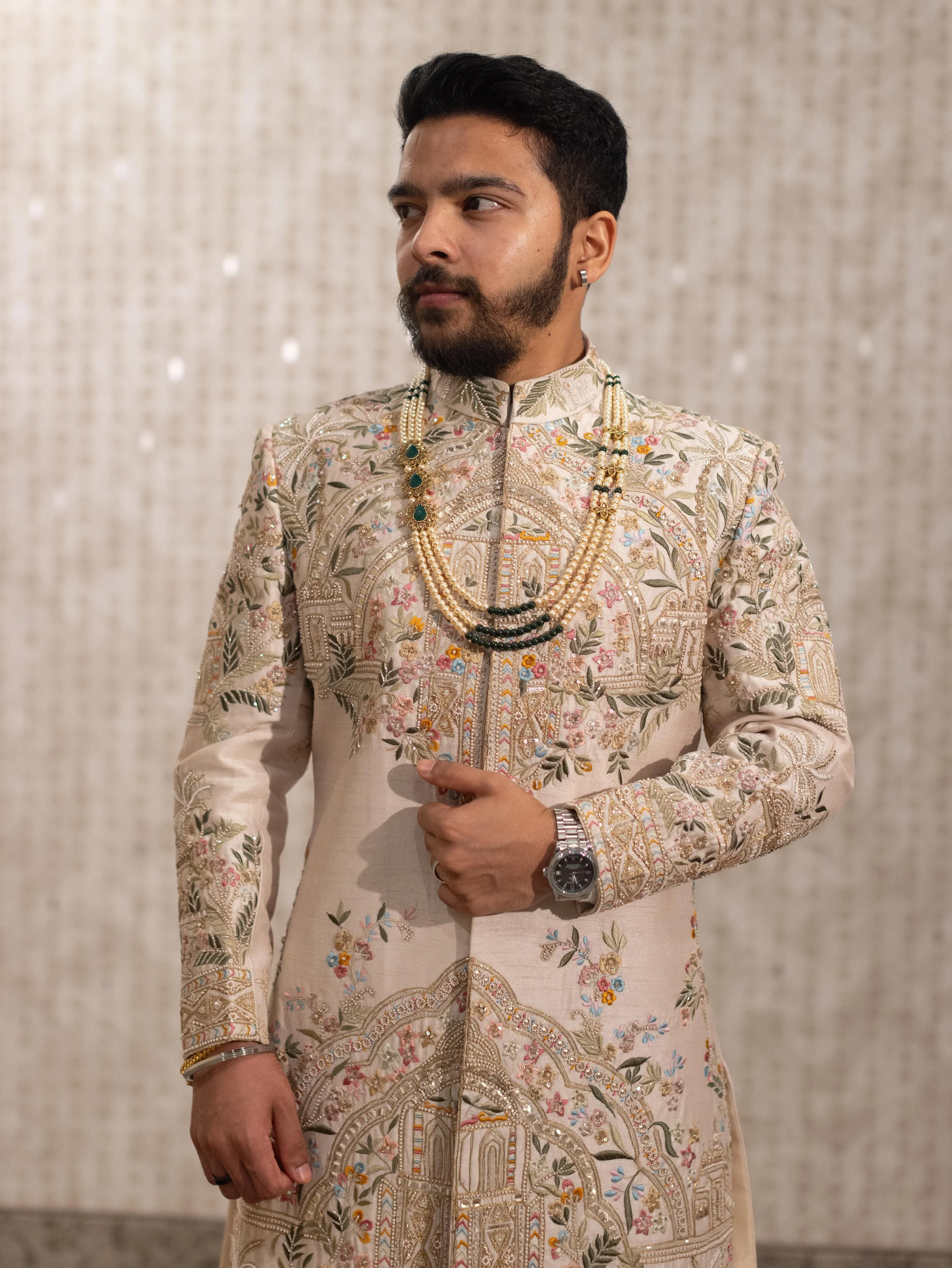Groom wearing a traditional Indian groom's sherwani with intricate embroidery, jewelry, and a watch.