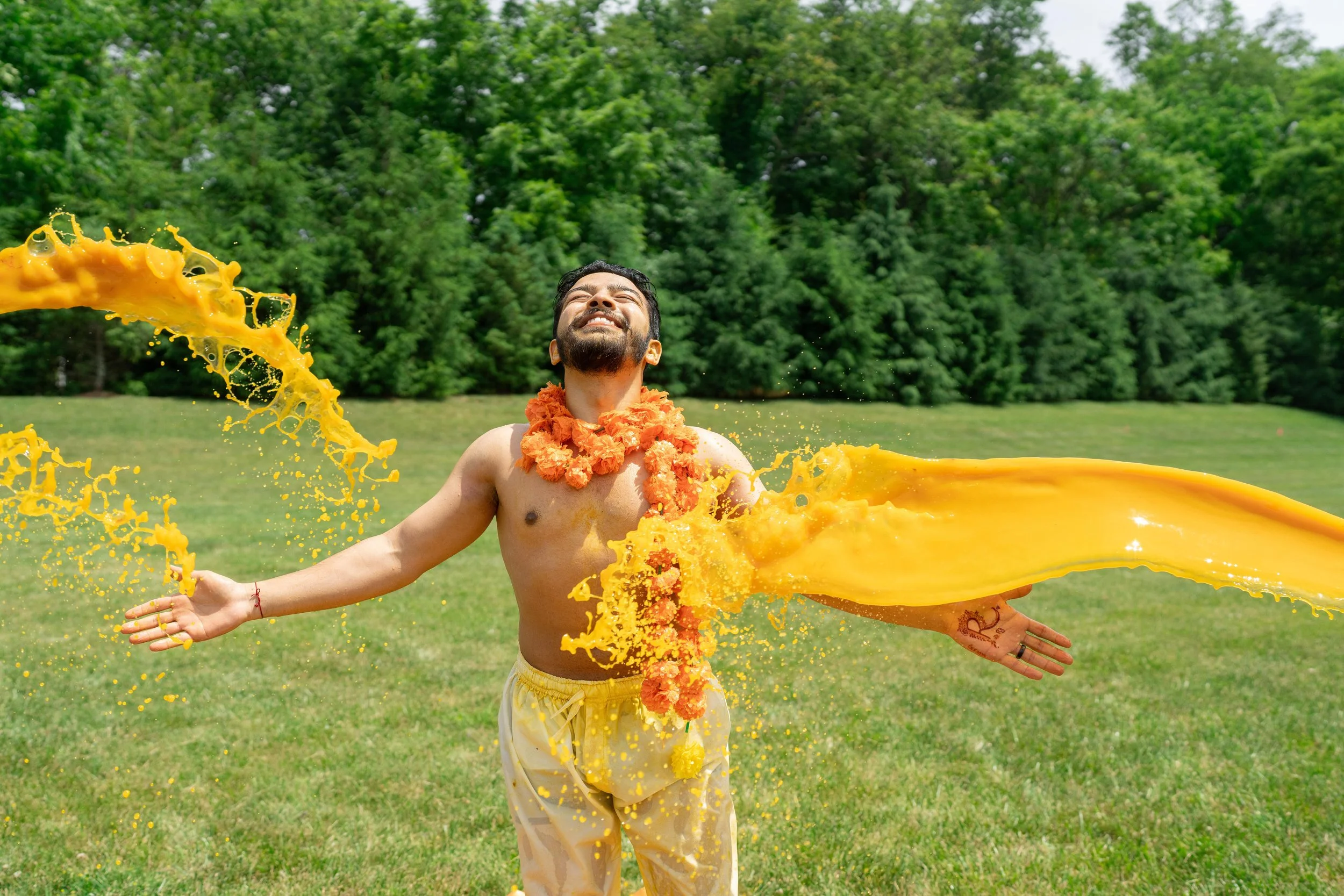 A groom with a flower garland around his neck, wearing yellow tumeric water, This is a fun rituals during Hadi/Pithi time.