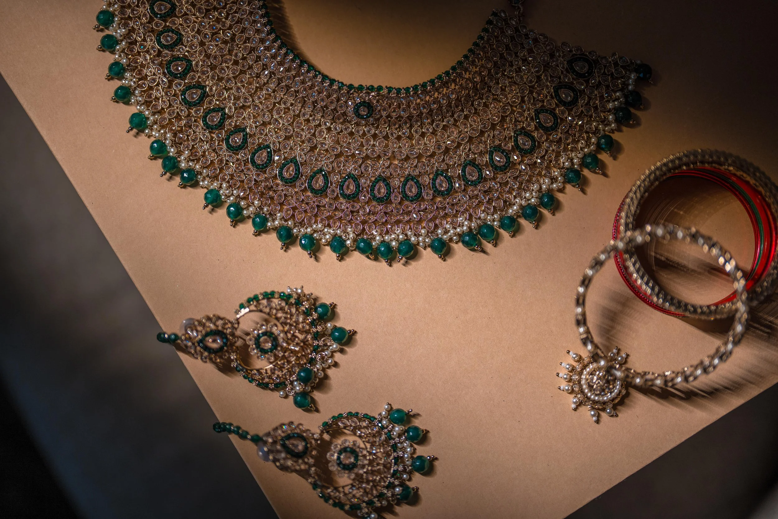 Jewelry display showing a large, ornate necklace, matching earrings, and bangles, all decorated with pearls and green gemstones.