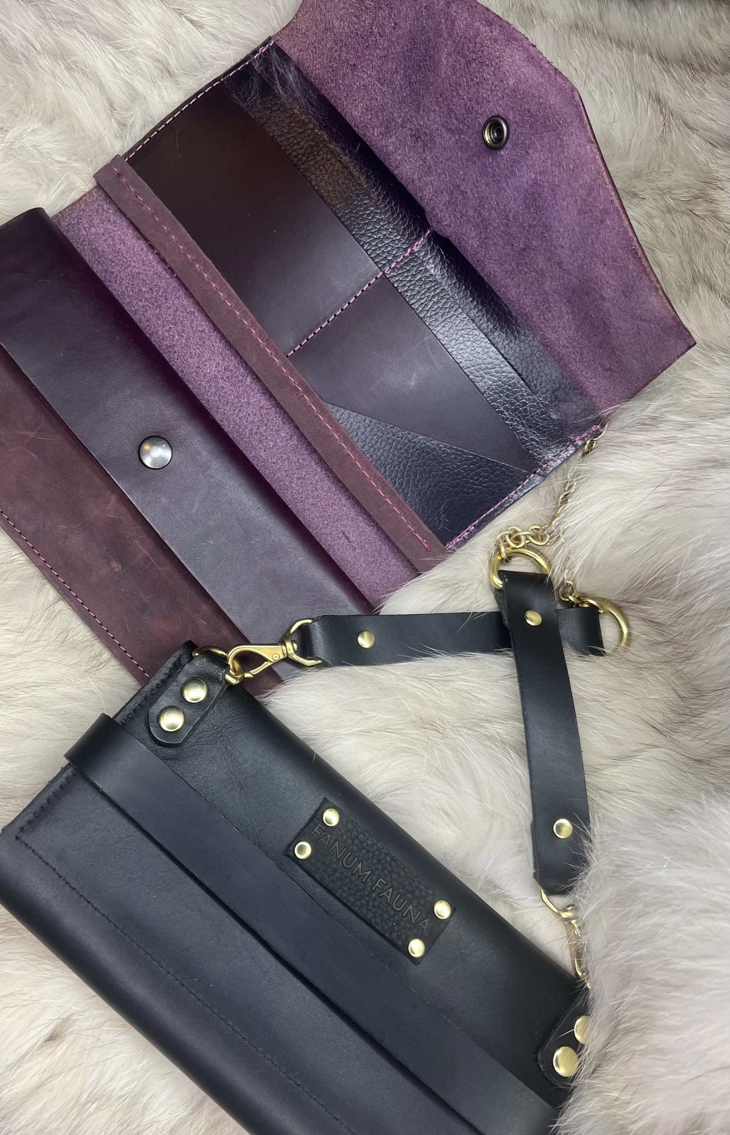 A leather purse with a purple suede interior and gold hardware, resting on a light-colored fur surface.