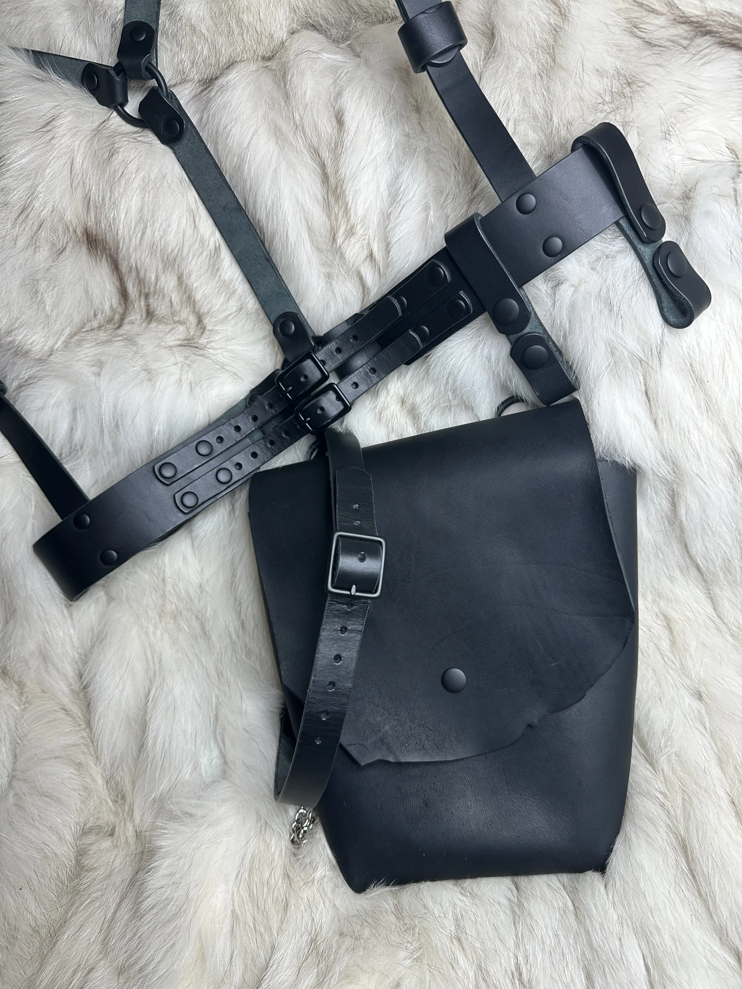 A black leather purse with metal hardware, placed on a plush white fur surface.