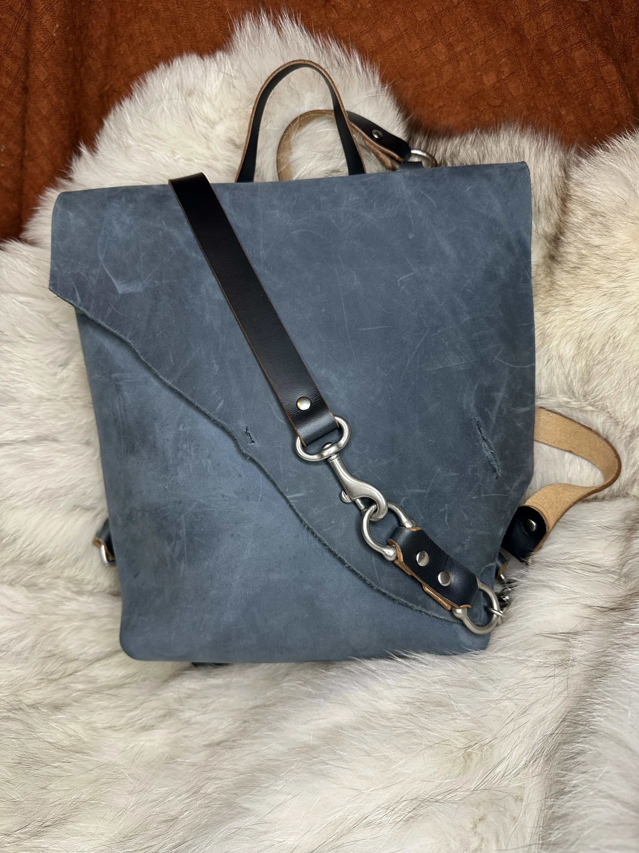 A blue leather tote bag with black and tan straps, placed on a white and brown furry surface.