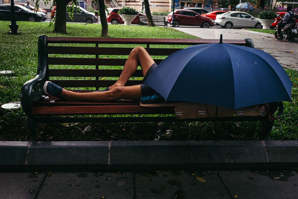 Man sleeping under an umbrella in a park in Hanoi