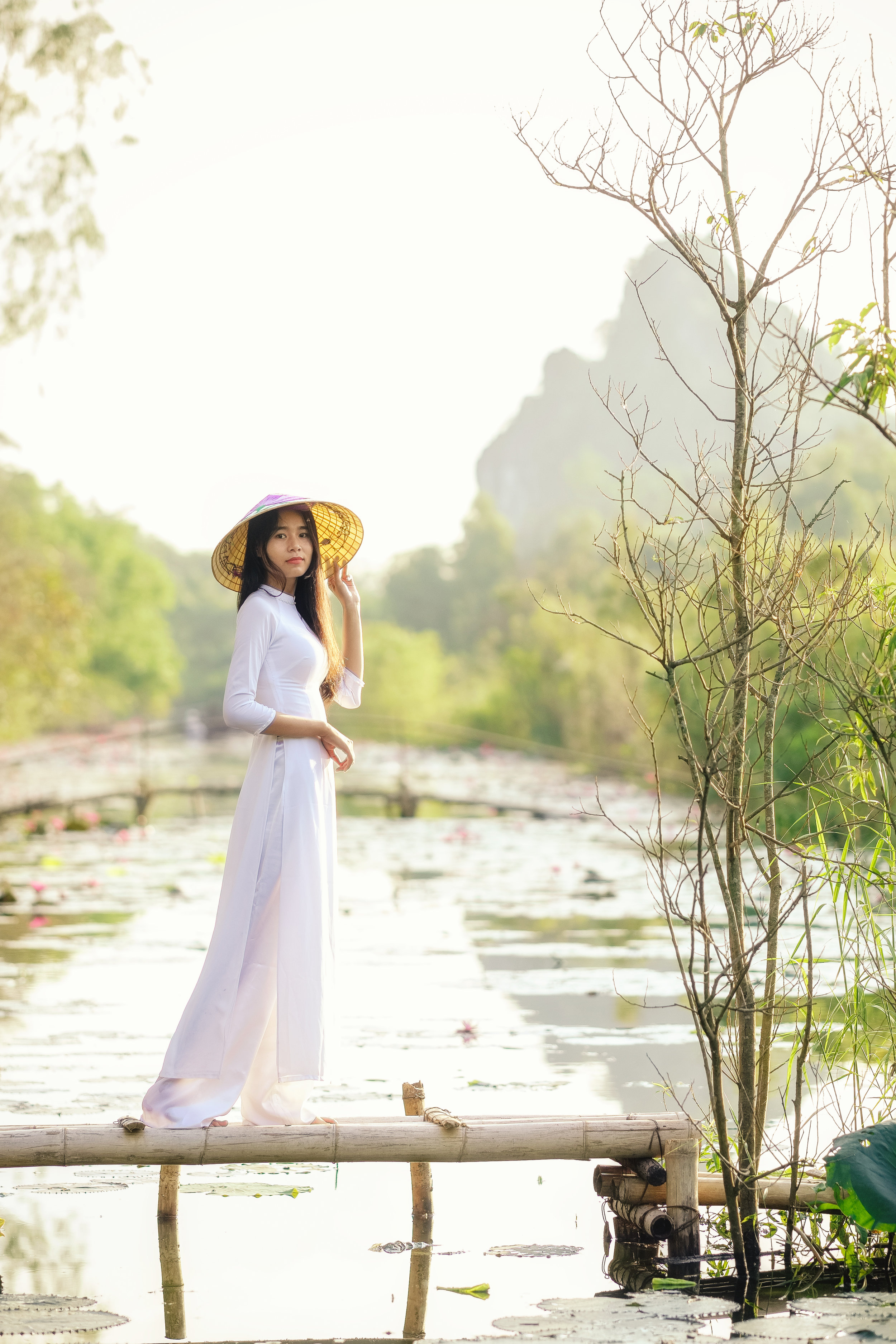 Vienamese girl in white ao dai dress standing on a wooden bridge