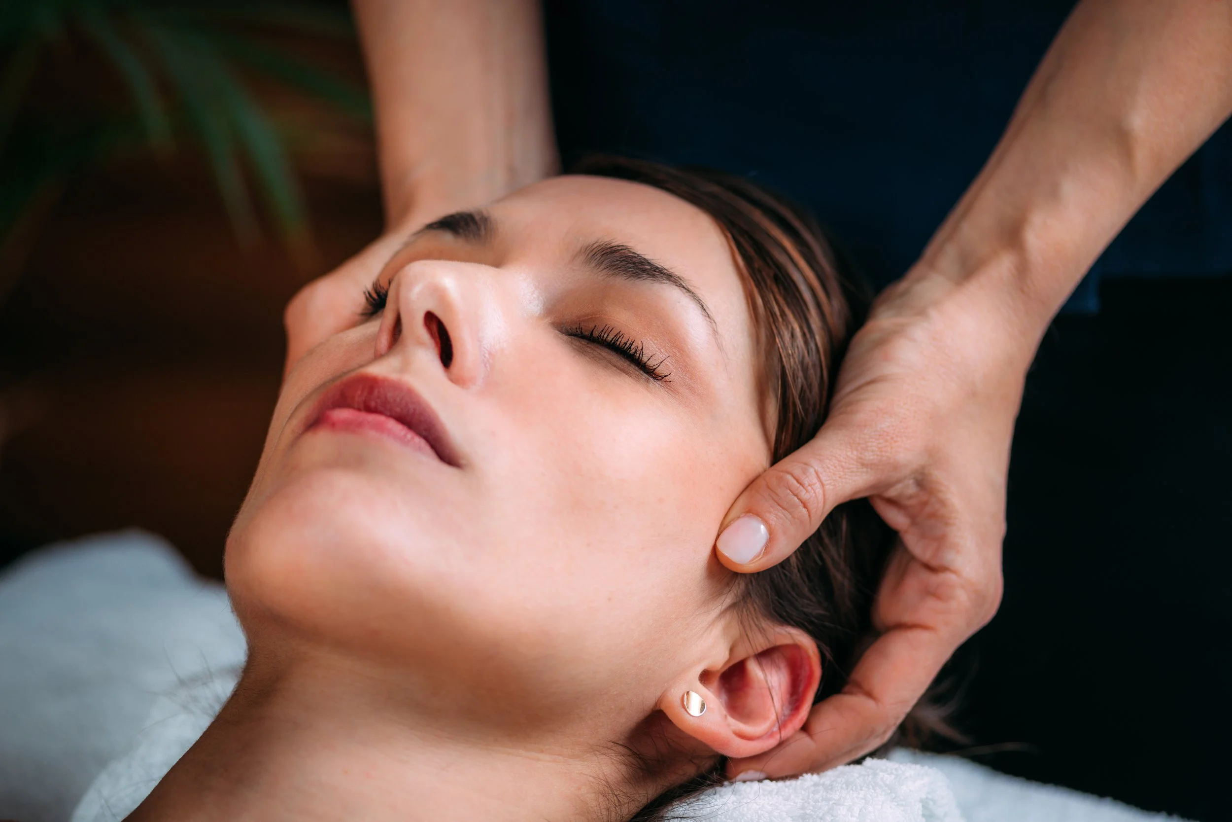 Woman receiving a head massage or spa treatment, lying down with eyes closed, with hands gently supporting her head.