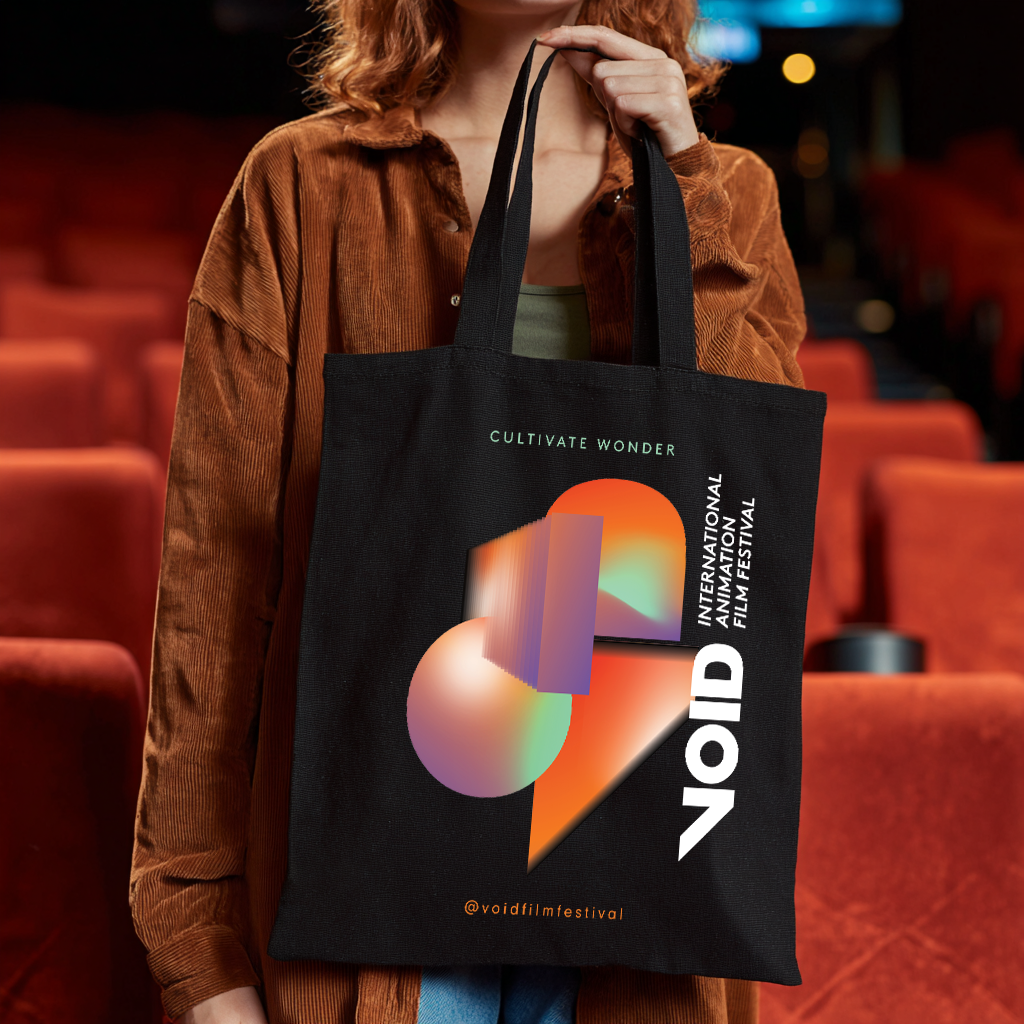 En person i en biograf med en sort totebag med farverigt design og teksten 'VOID', der promoverer International Animation Film Festival.