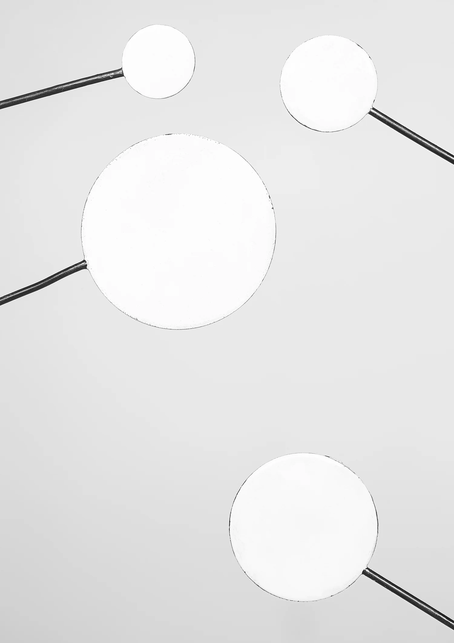 Black and white image of four circular lights connected by rods, with two on the top and two on the bottom, set against a plain light background.