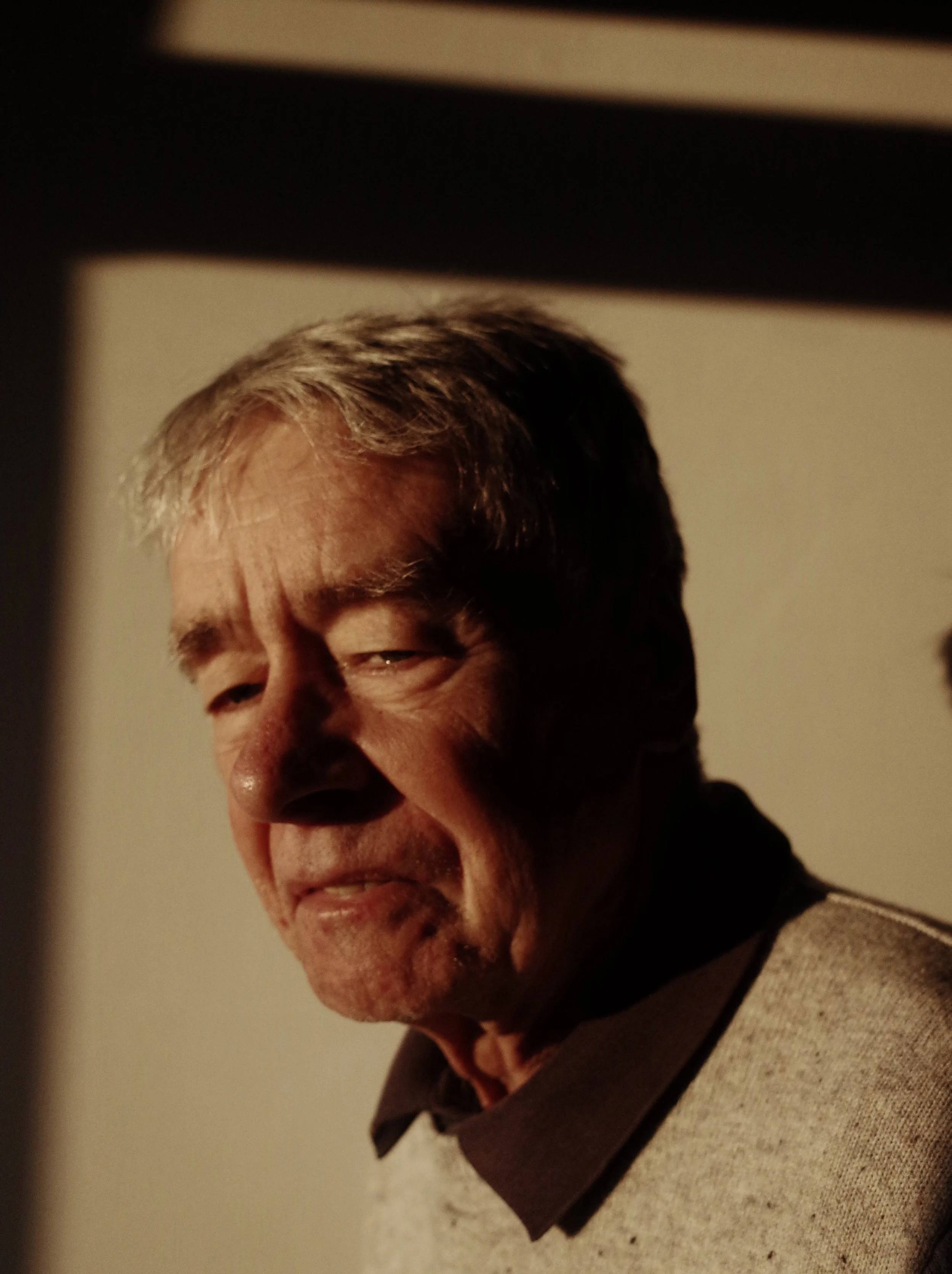 A middle-aged man with gray hair, smiling slightly, with his face lit warmly from the side, against a neutral background.