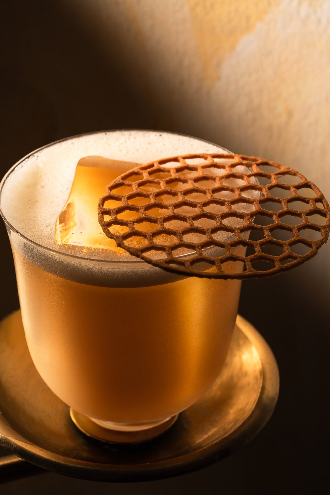 A glass of creamy latte with foam, topped with a slice of butter and a decorative cookie.