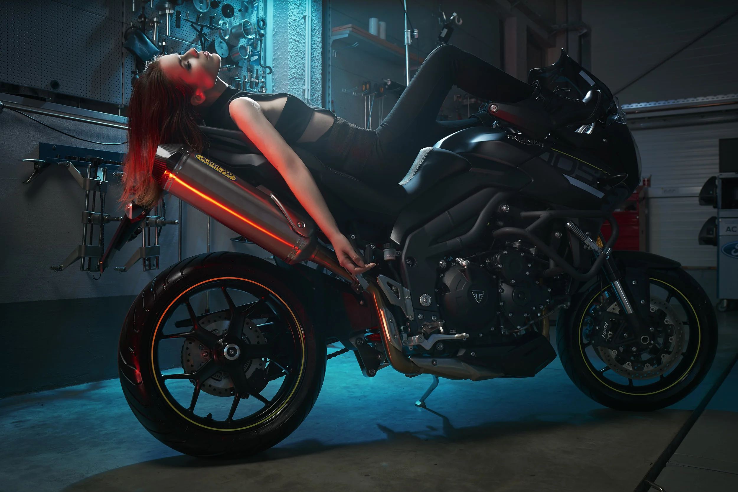 A girl laying on a motorcycle in the garage, photographed by Baywer.