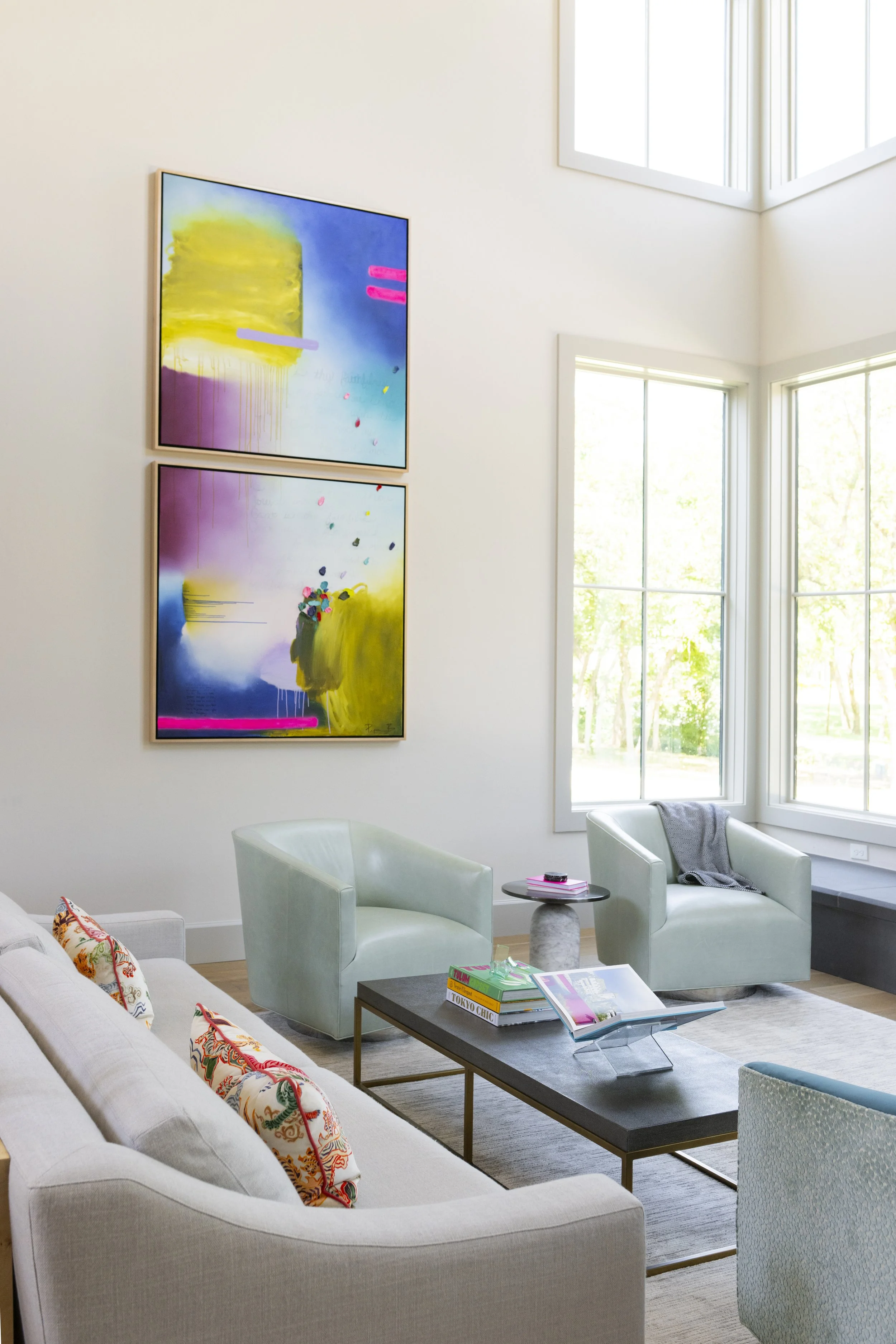 Luxury living room design with tall windows, colorful abstract art, pale blue armchairs, a neutral sofa, and a modern coffee table.