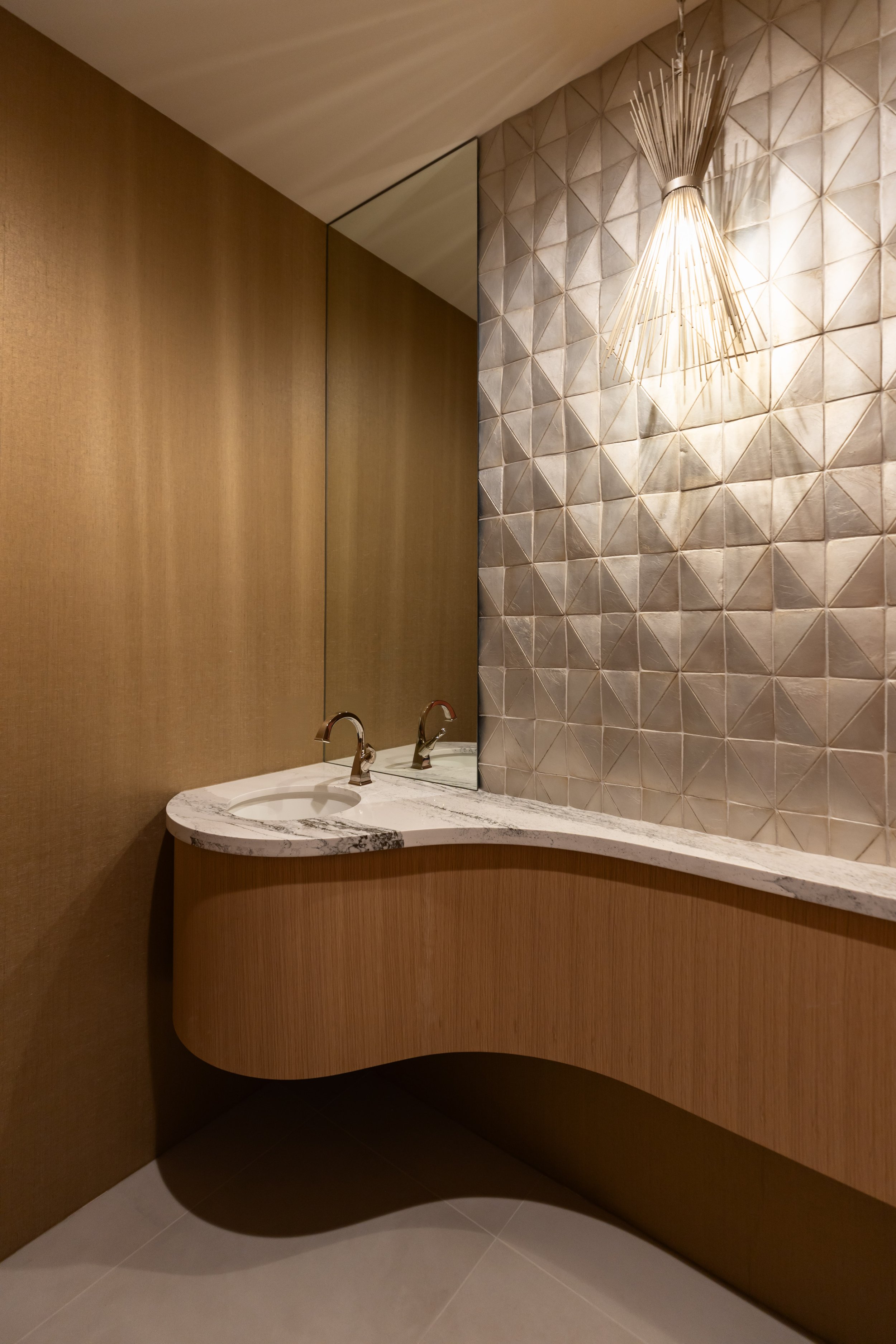 Powder room with curved wood vanity, dimensional feature wall and natural stone countertop