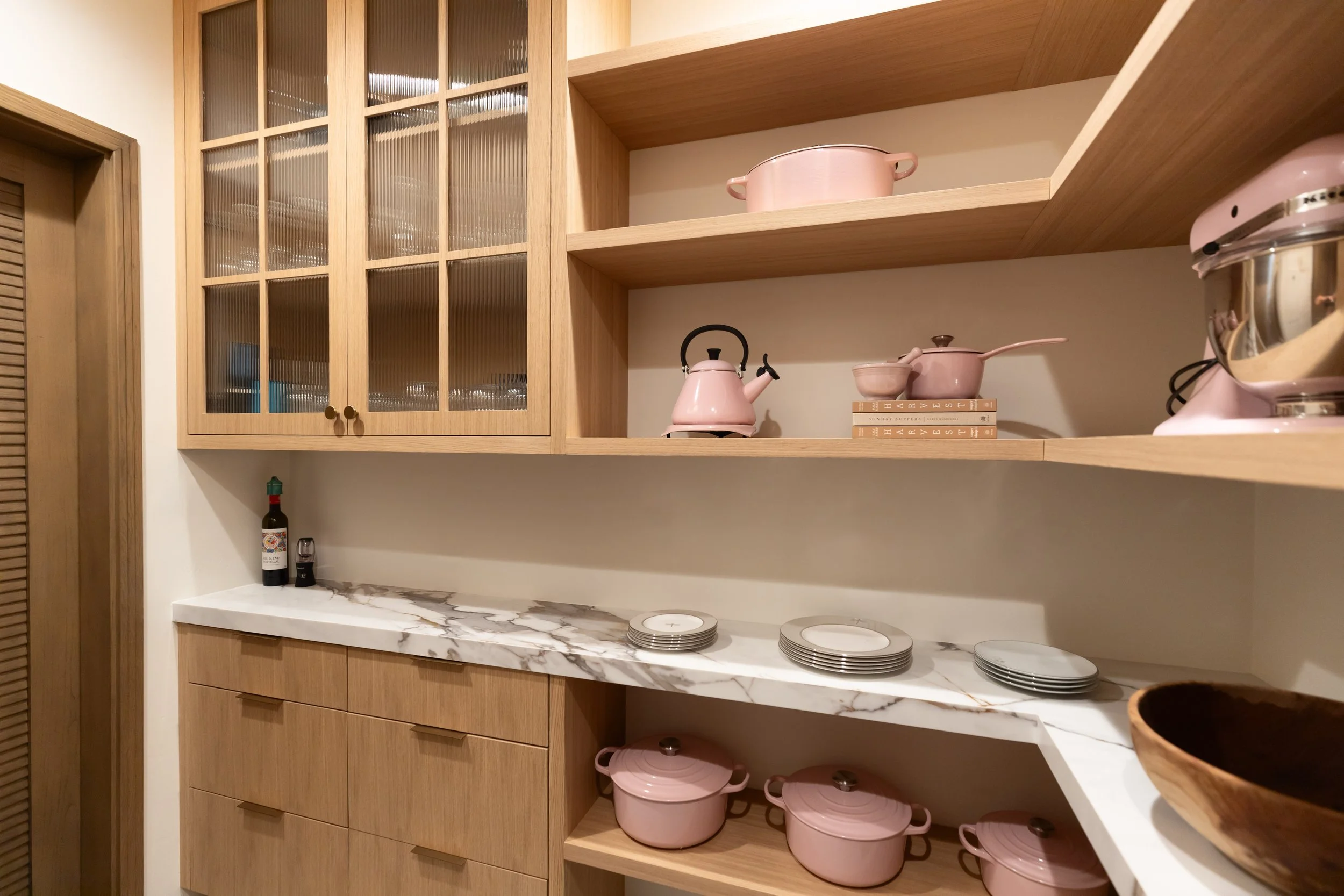 Custom walk-in pantry with warm wood cabinetry, glass-front uppers, open shelving and stone countertops