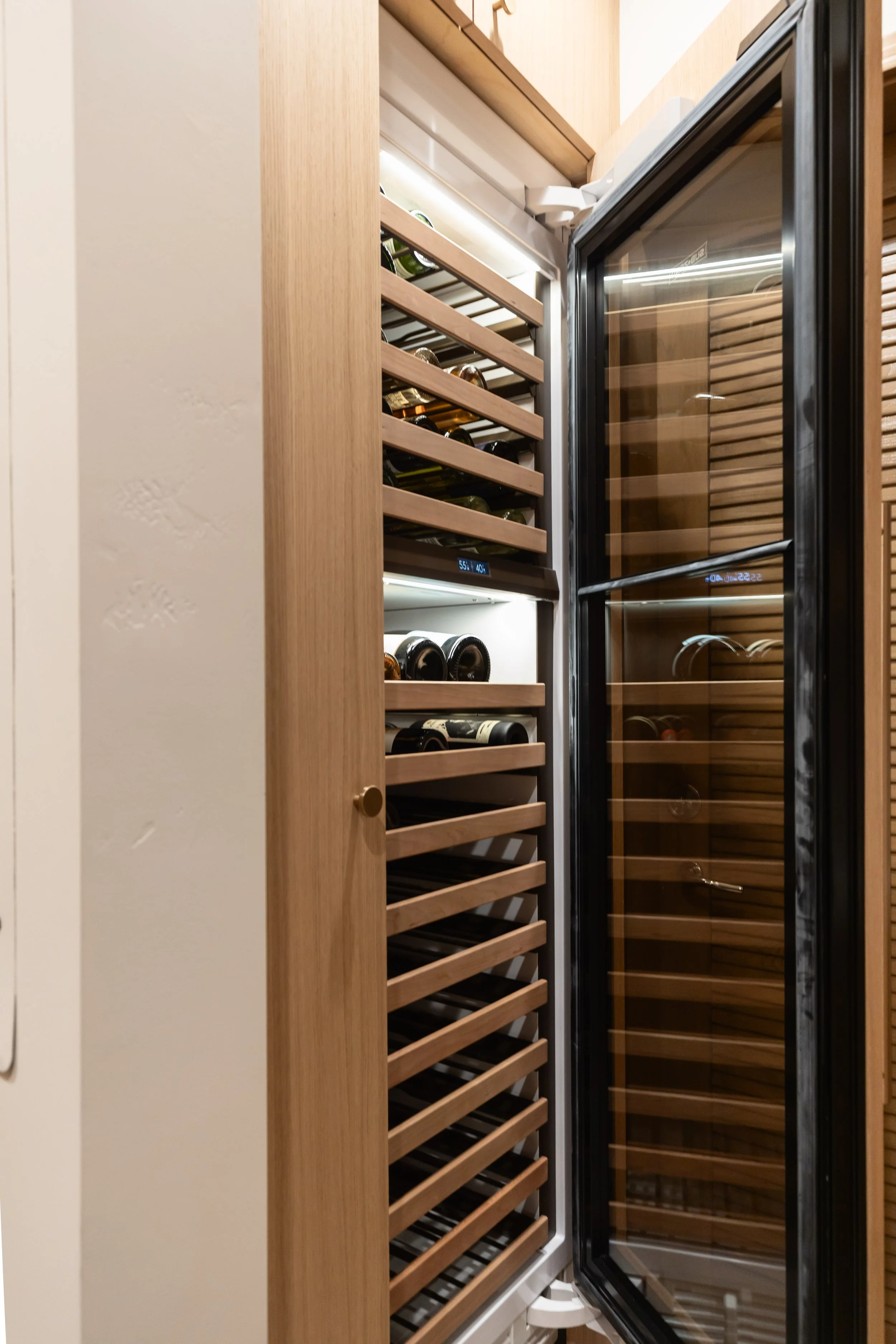 Integrated wine storage tucked behind dark louvered doors beside the custom kitchen and pantry