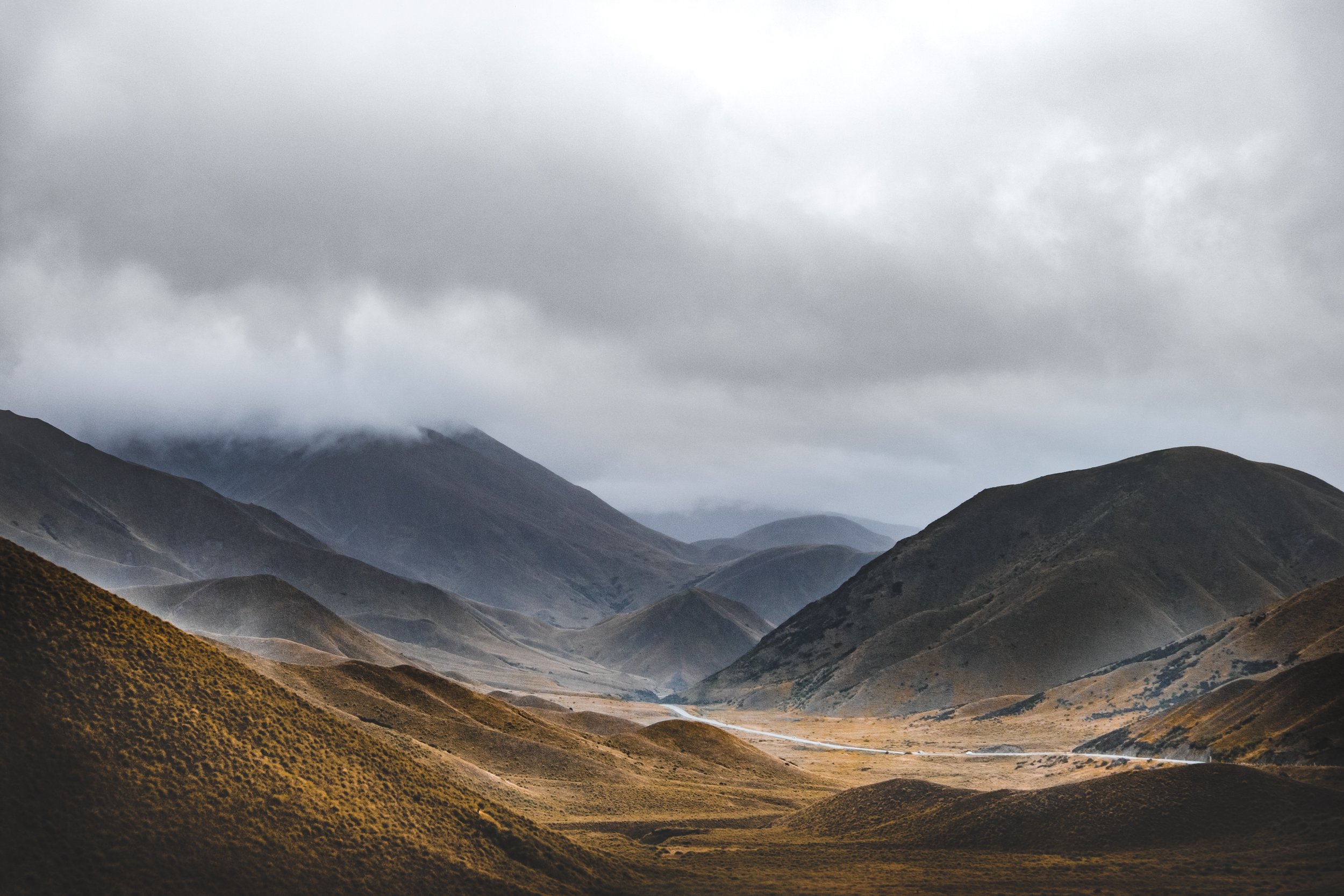 Mountain landscape with rolling hills, cloudy sky, and mist-covered peaks in the distance.