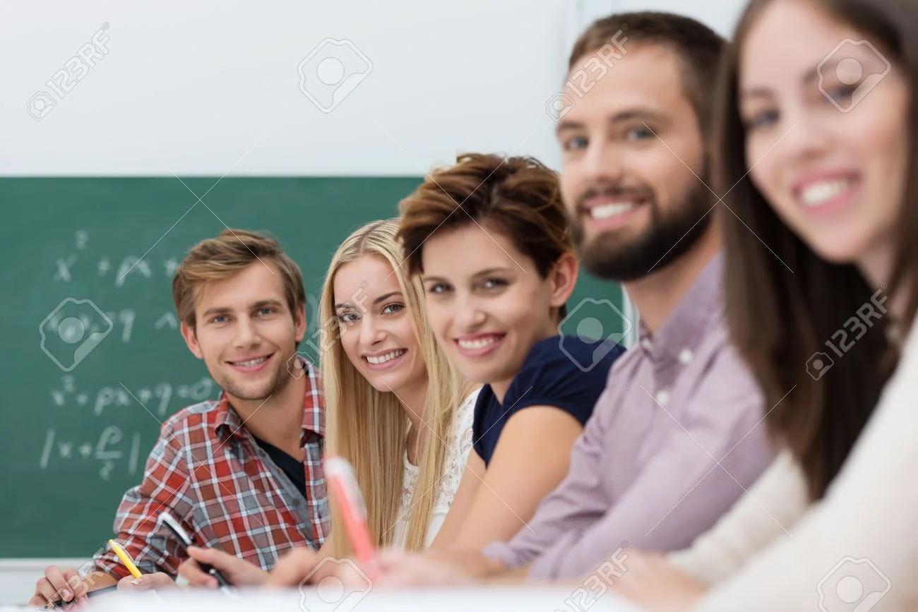 22250117-diverse-group-of-contented-happy-university-students-sitting-in-a-row-at-a-long-table-in-the-classro.jpg