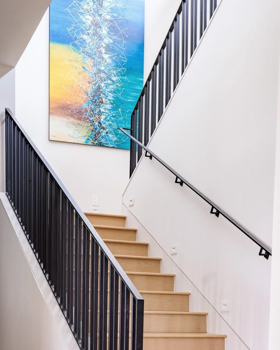 We love the modern black railing and the clean lines of our client&rsquo;s stairwell. The impressive colorful art draws your eye upward. Who says a staircase has to be boring?