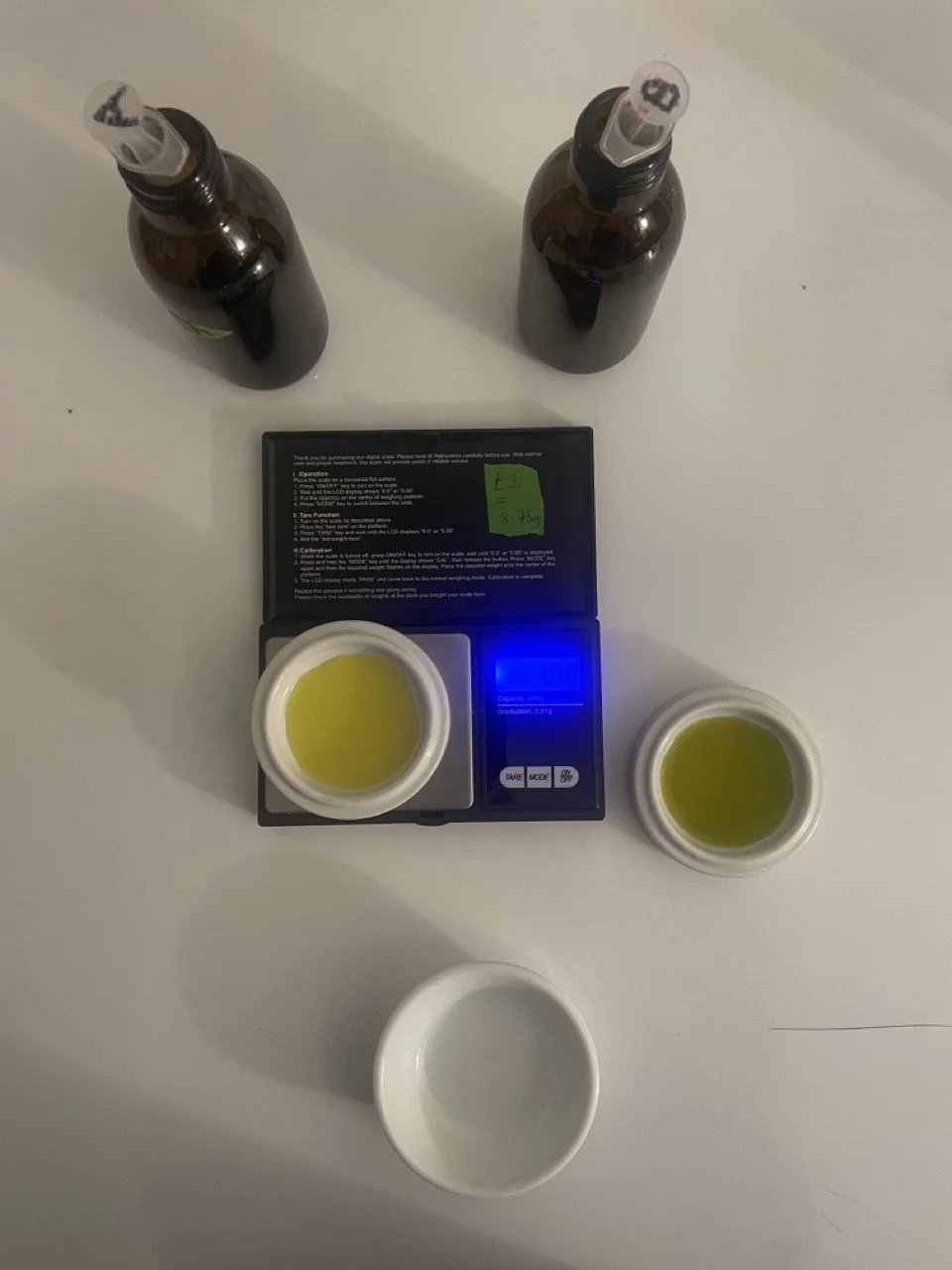 To brown bottles with syringes in them - two ceramic dishs containing yellow cyanotype chemicals, one is on digital scales and one on the table - from visual artist Harri Harrison Grief Commissions-