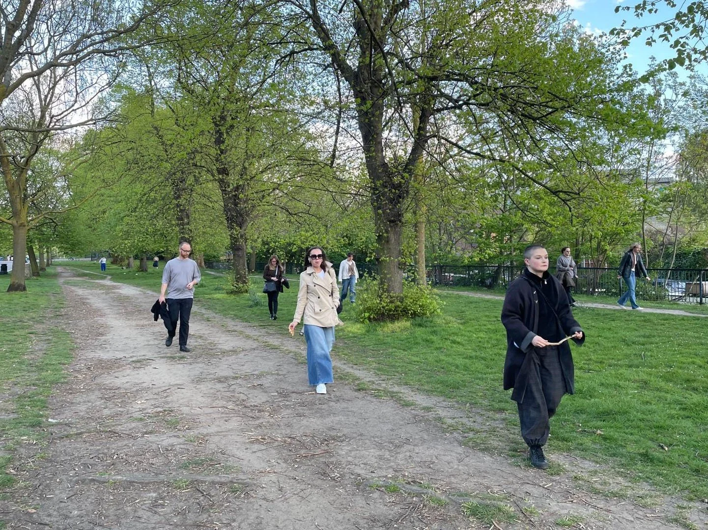 Harri Harrison walking at the front of a group in Victoria Park, holding a stick, with participants following behind on informal paths.
